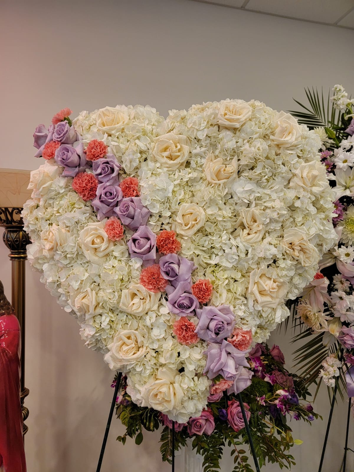 Large heart-shaped standing arrangement of white flowers with lavender roses and coral carnations on an easel