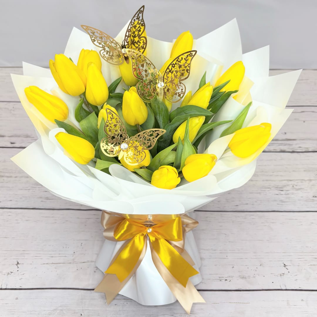 Bouquet of yellow tulips wrapped in white paper with gold butterfly picks
