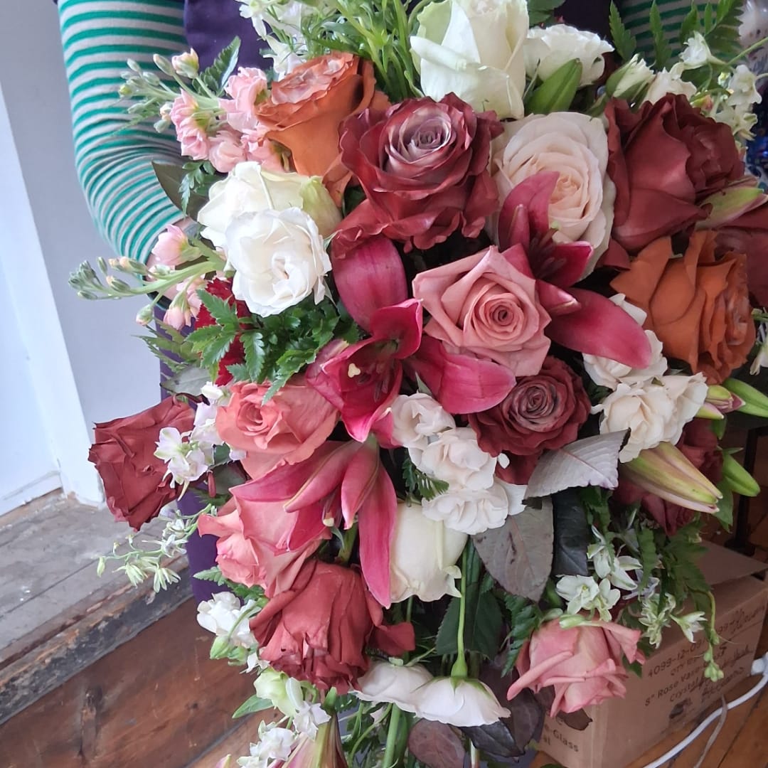 Large bouquet of roses, lilies, and white filler flowers in mixed pink, red, and cream tones