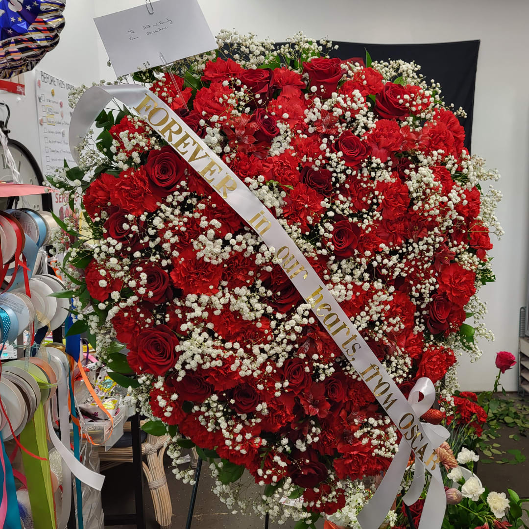 Large heart-shaped red rose and carnation arrangement with a white ribbon