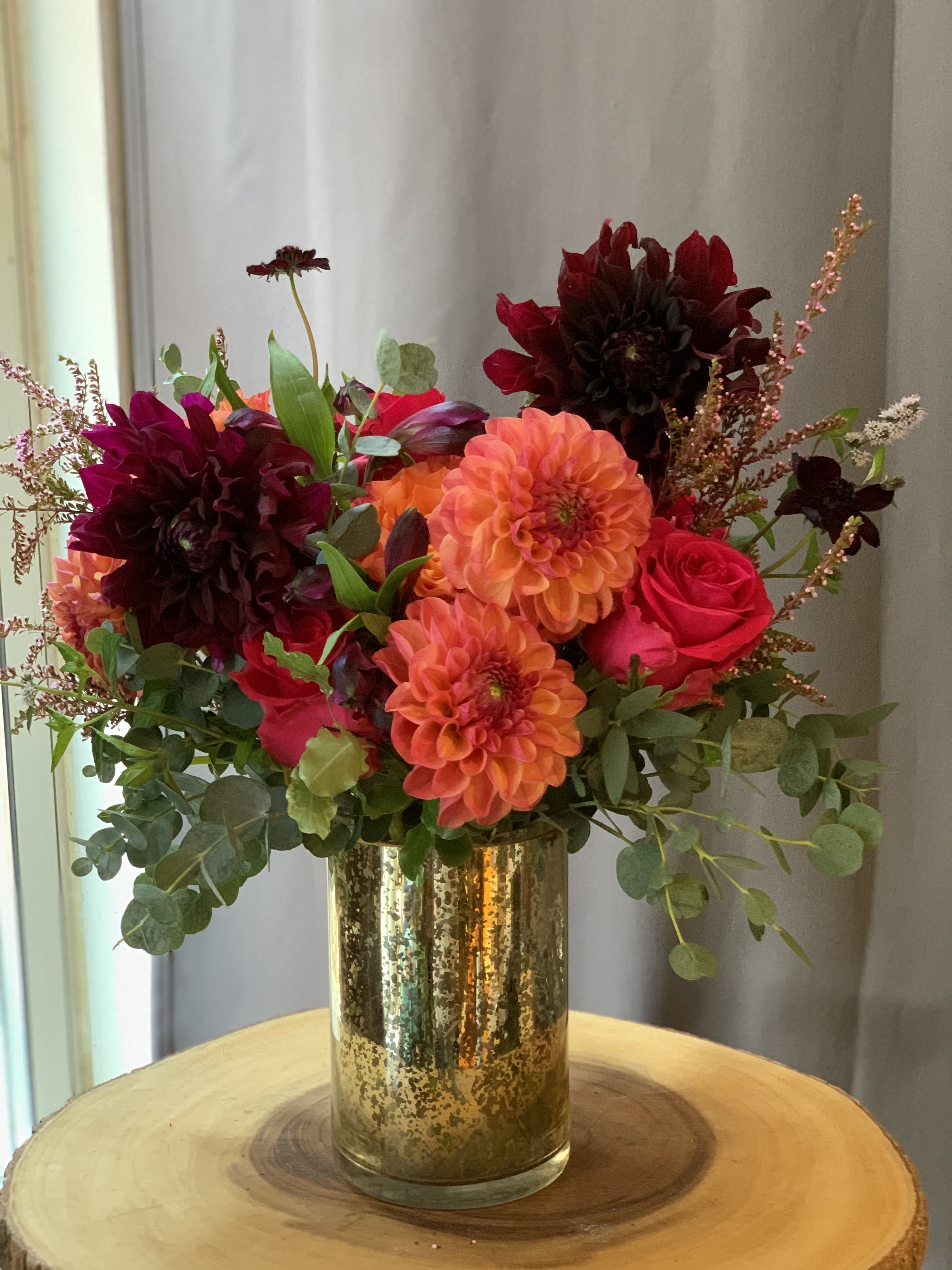 Bright mixed bouquet in a gold vase with orange, red, and dark burgundy blooms