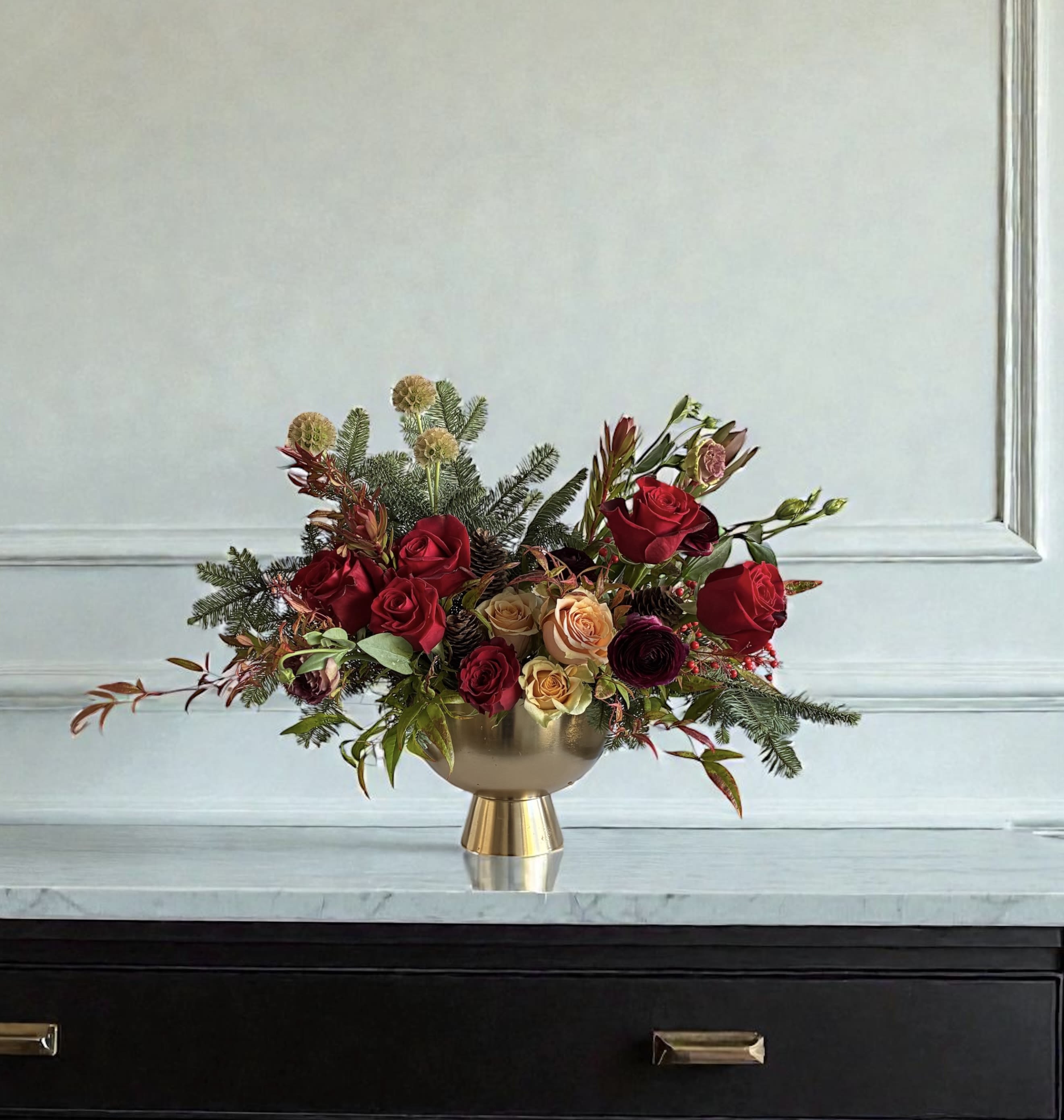 Winter Glow - A rich and refined arrangement designed to bring instant elegance to any space featuring velvety reds, warm toned blooms and textural winter greens. Styled in a chic gold vessel. It's perfect for holiday tables, and gifting someone who loves sophisticated floral design. Colors and flowers may vary based on availability.  Color options are red/peach or red/white. Please state in special instructions or call in to order.   Pictured in Premium.   For same day delivery contact us at 949-682-5004 