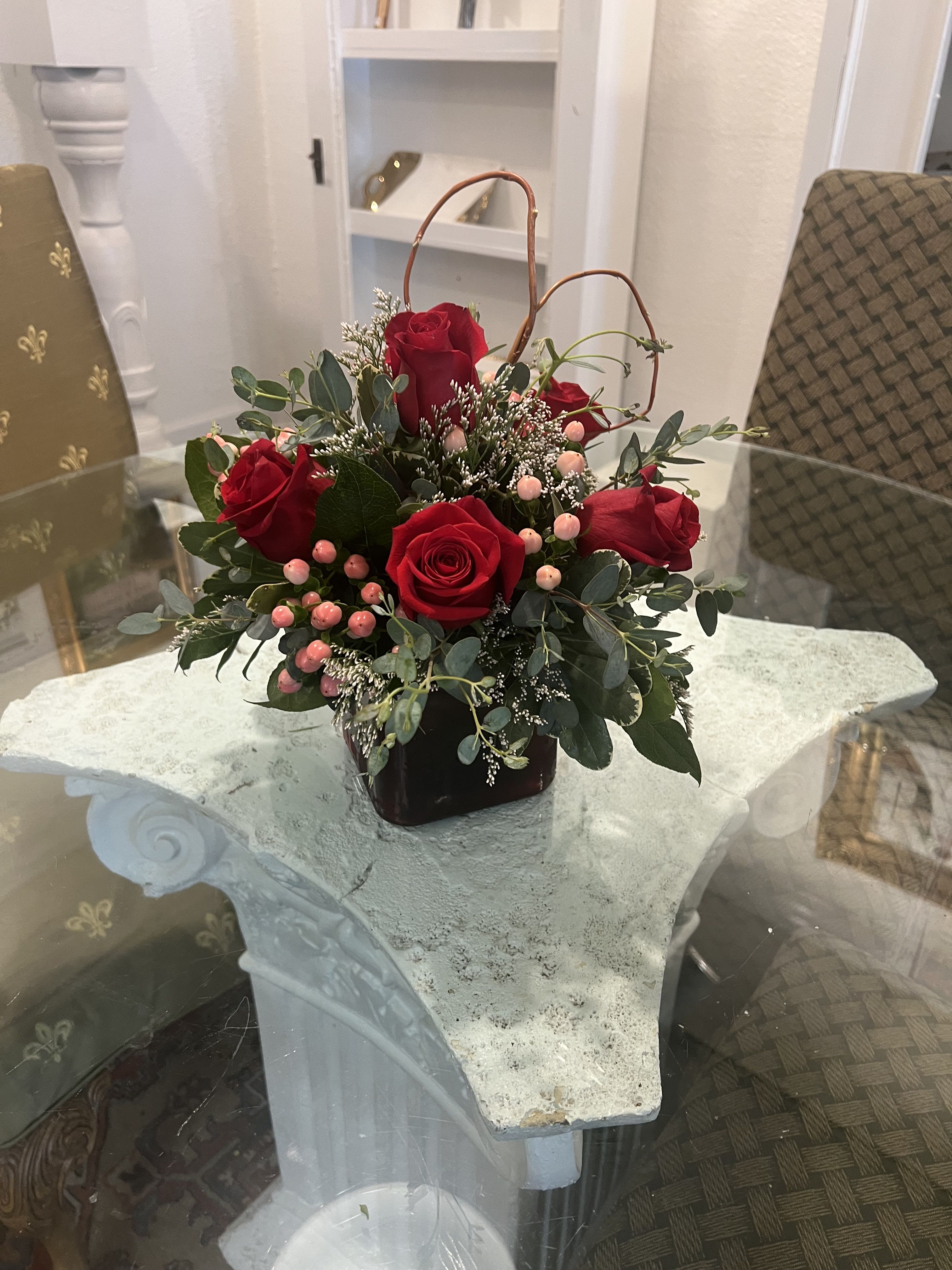 Red roses arranged in a dark vase with pink berries and greenery