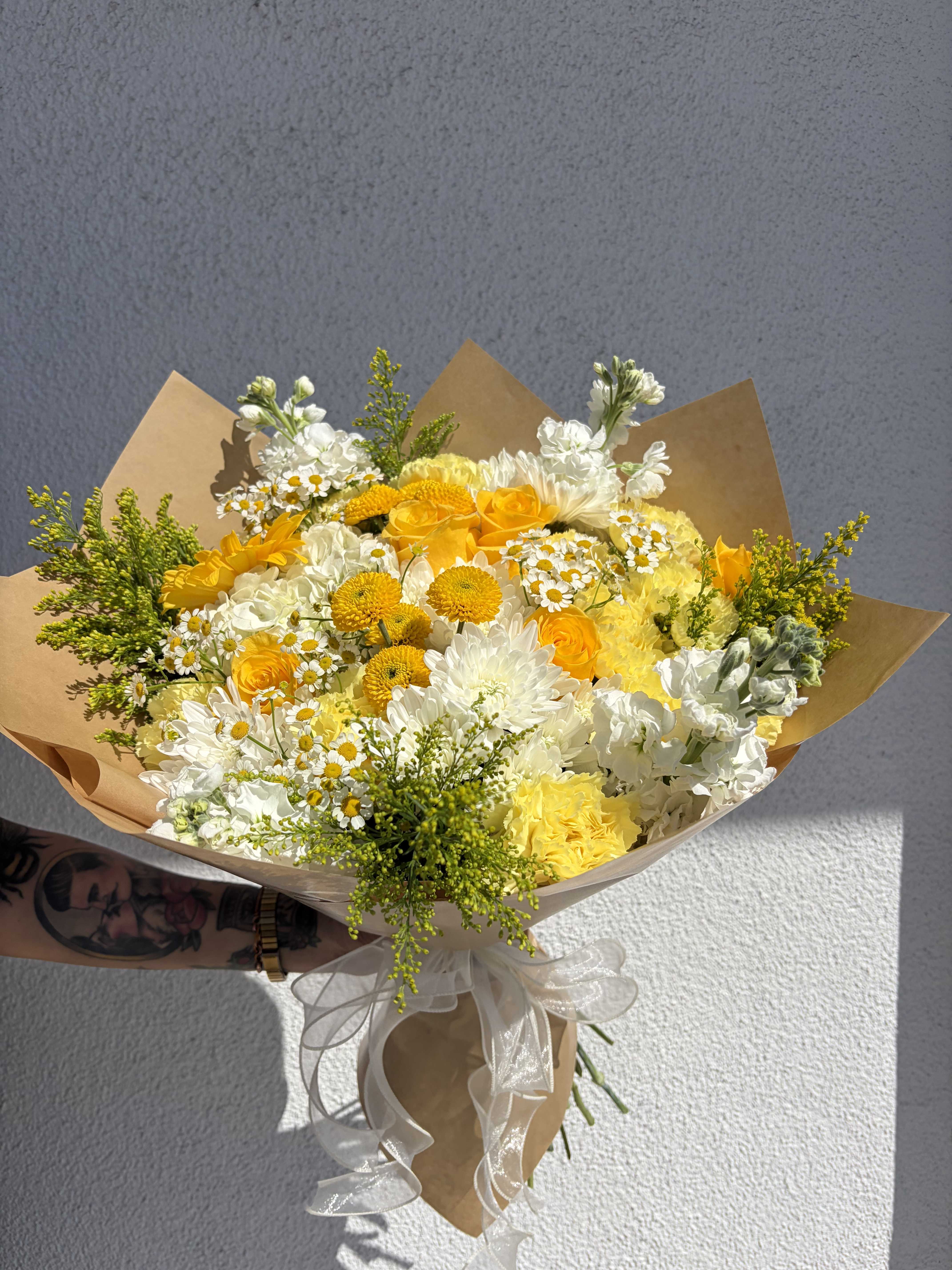 Yellow and white mixed bouquet wrapped in brown paper with a white ribbon