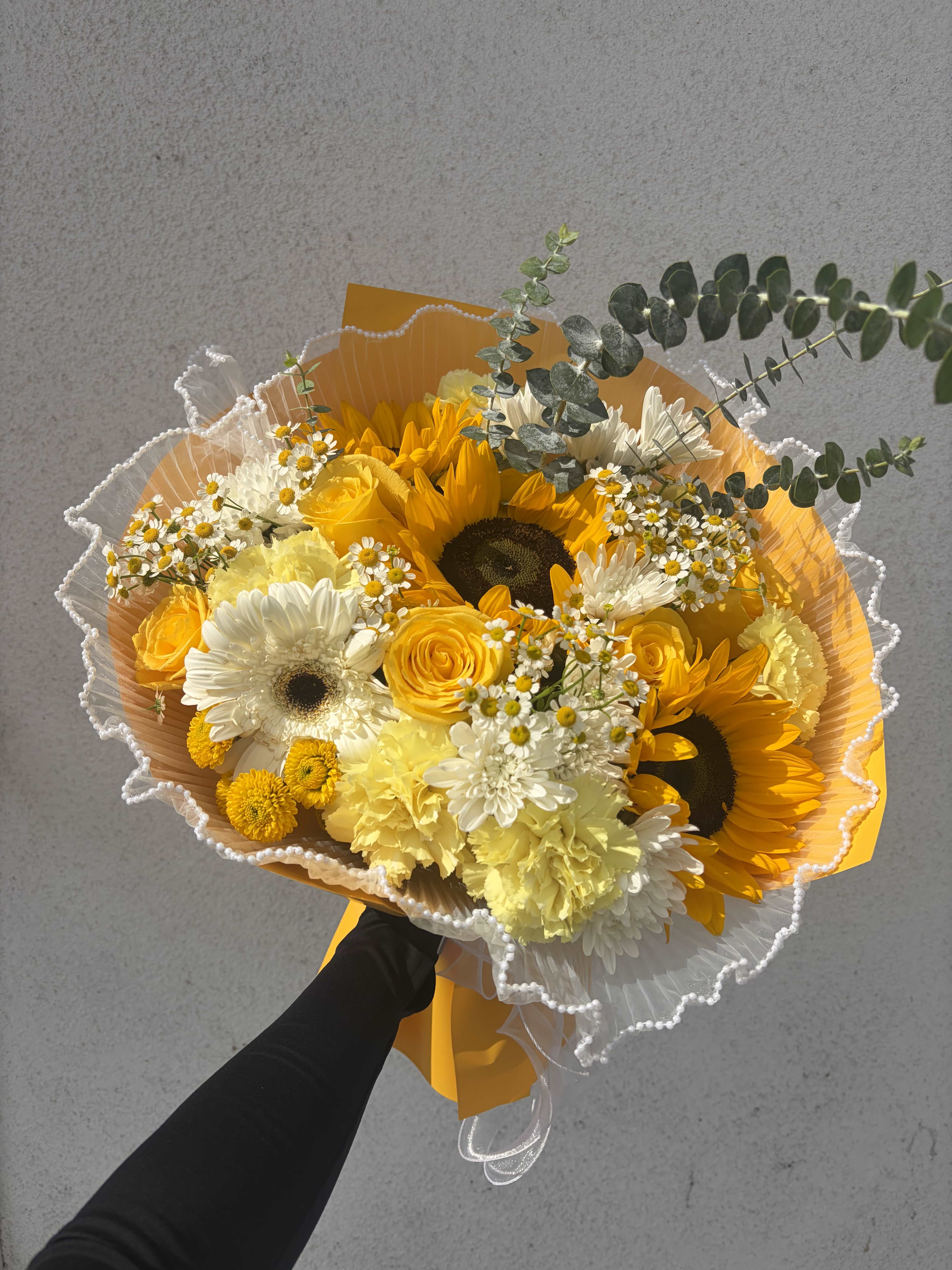 Bouquet of yellow sunflowers, roses, and white daisies wrapped in orange paper