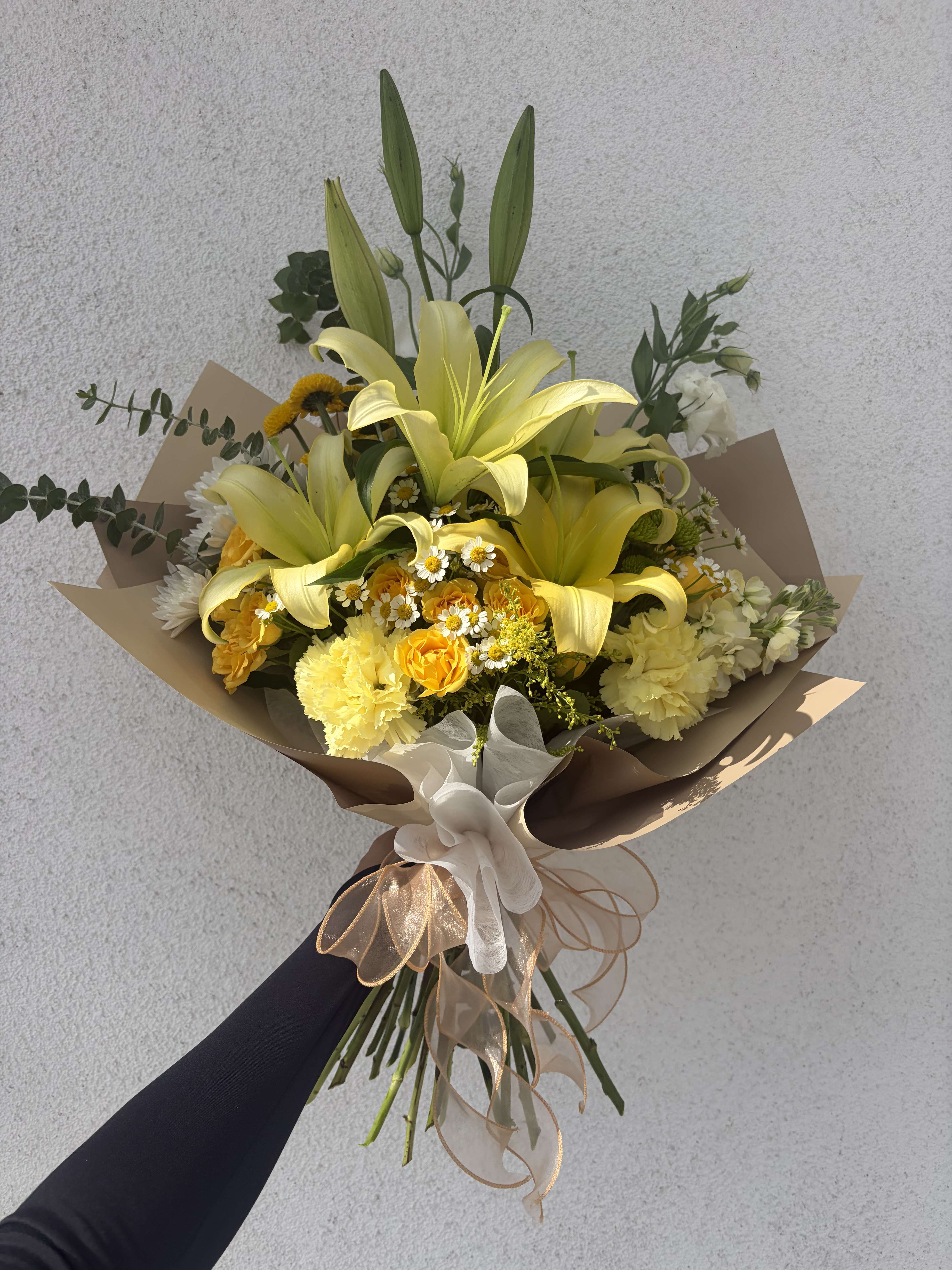 Yellow lily bouquet with mixed flowers wrapped in brown paper and ribbon