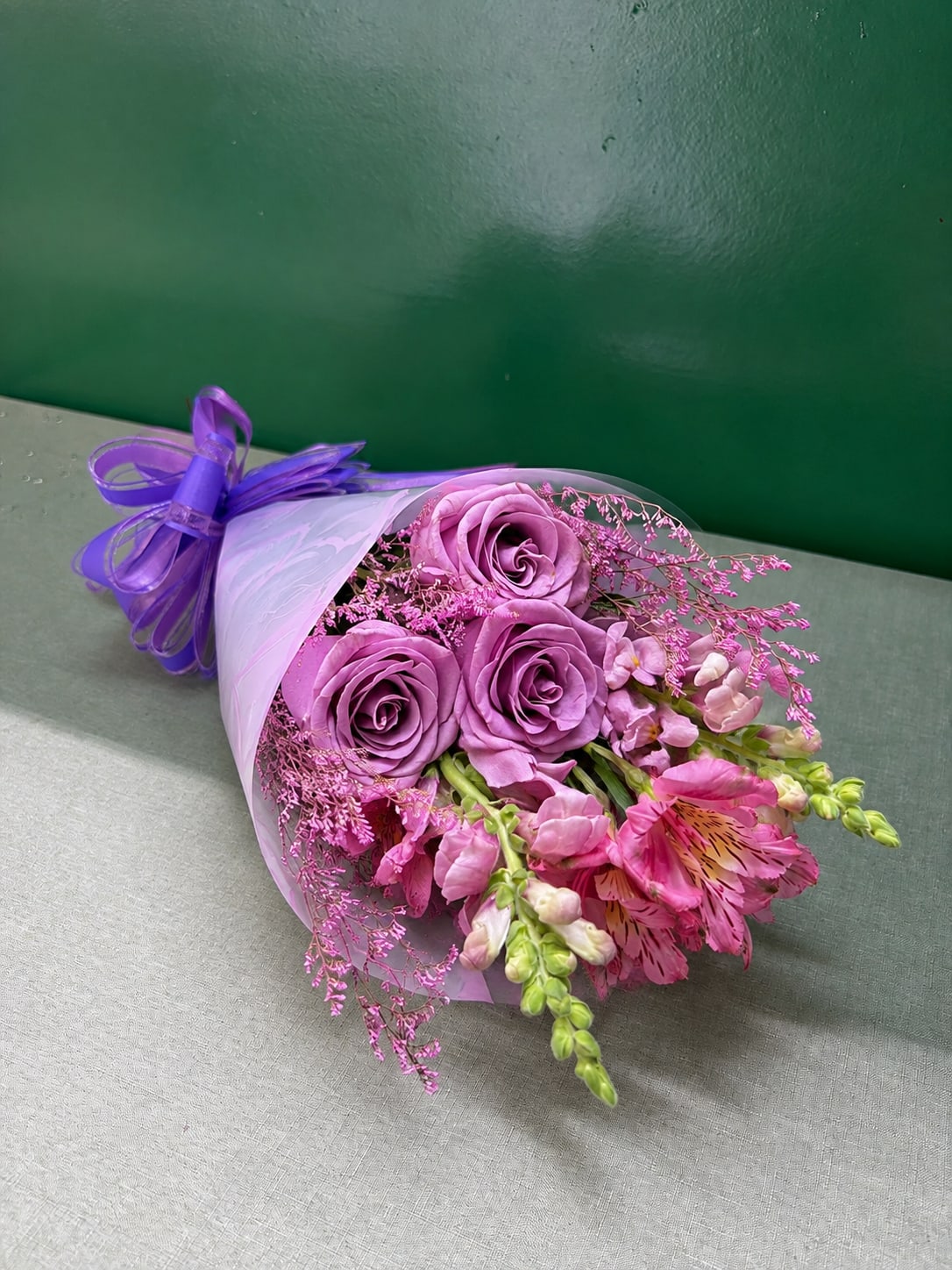 Bouquet of lavender roses and pink flowers wrapped in white paper with a purple ribbon