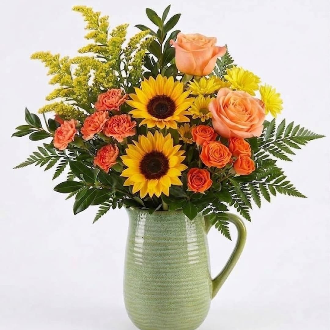 Bouquet of sunflowers, peach roses, and orange carnations in a green ceramic pitcher