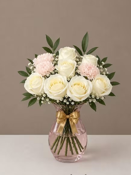 Blush Rose Ivory Vase - Choose a soft, romantic centerpiece that feels both personal and polished - a vase arrangement of roses, carnations, hydrangeas, and calla lilies, perfect for a birthday, anniversary, or a just-because "thinking of you" surprise. Whether you prefer the pale, calming mix of white roses and pink carnations or the richer red-and-cream composition, each arrangement is designed to make the recipient feel truly seen and celebrated. These designs also read beautifully for thank-you notes or love-and-romance moments.  Each bouquet is hand-gathered into a rounded, full shape and presented in a clear or deep red glass vase finished with a satin gold ribbon or a wide black ribbon for a more formal look. Expect combinations of white roses, soft pink carnations, creamy hydrangeas, deep red roses, and dark burgundy calla lilies, accented with small white filler blooms and dark green, eucalyptus-like foliage for texture and lift. The result is an elegant, tactile mix of blooms and colors - white, pink, green, red, and touches of black ribbon - that complements both everyday gifting and milestone celebrations.