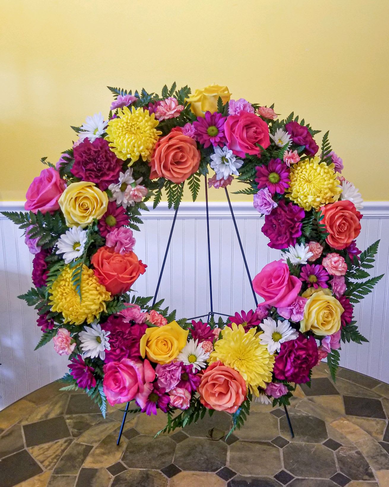 Large floral wreath on a stand with pink, yellow, white, and coral blooms