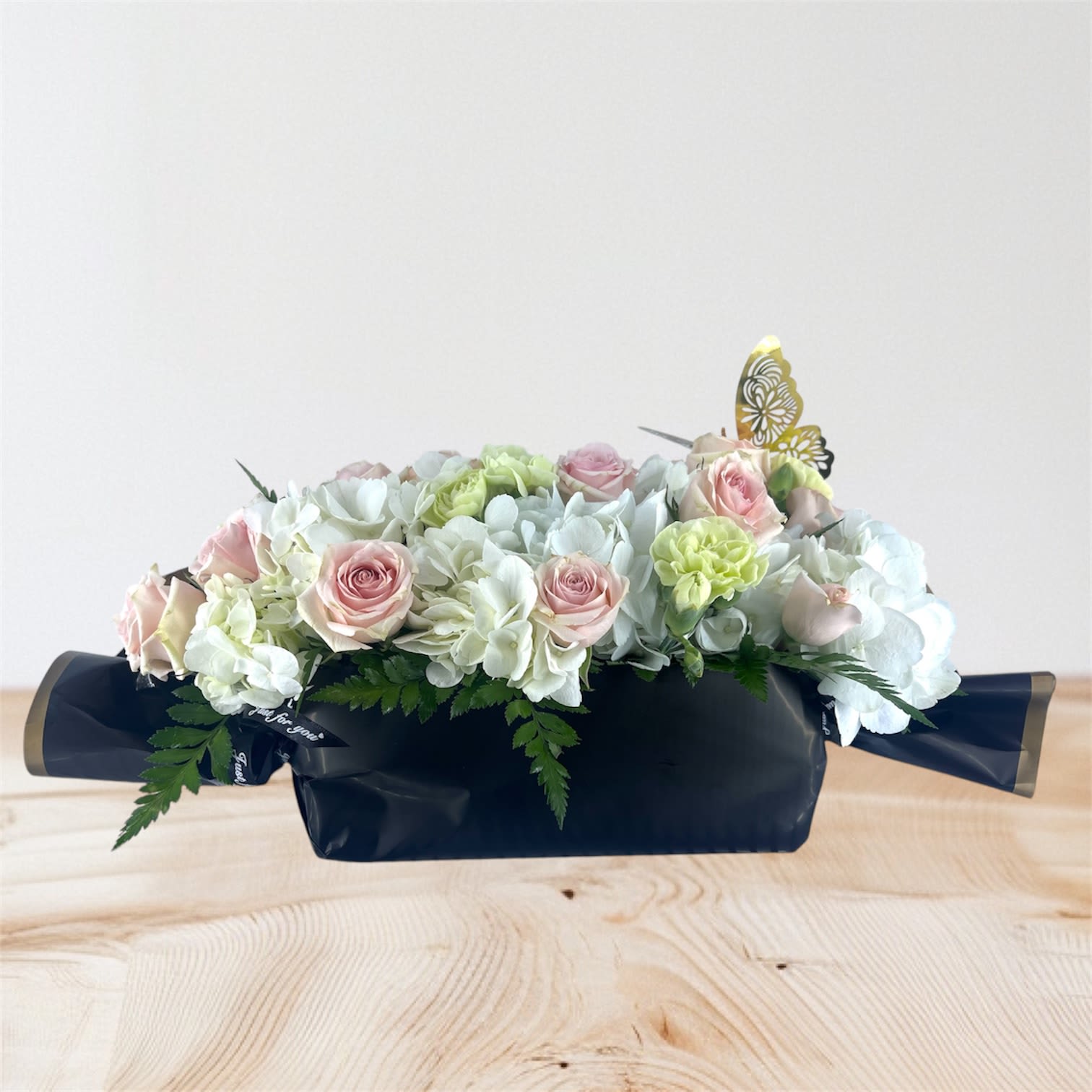 Pastel rose and hydrangea arrangement in a dark box with butterfly picks