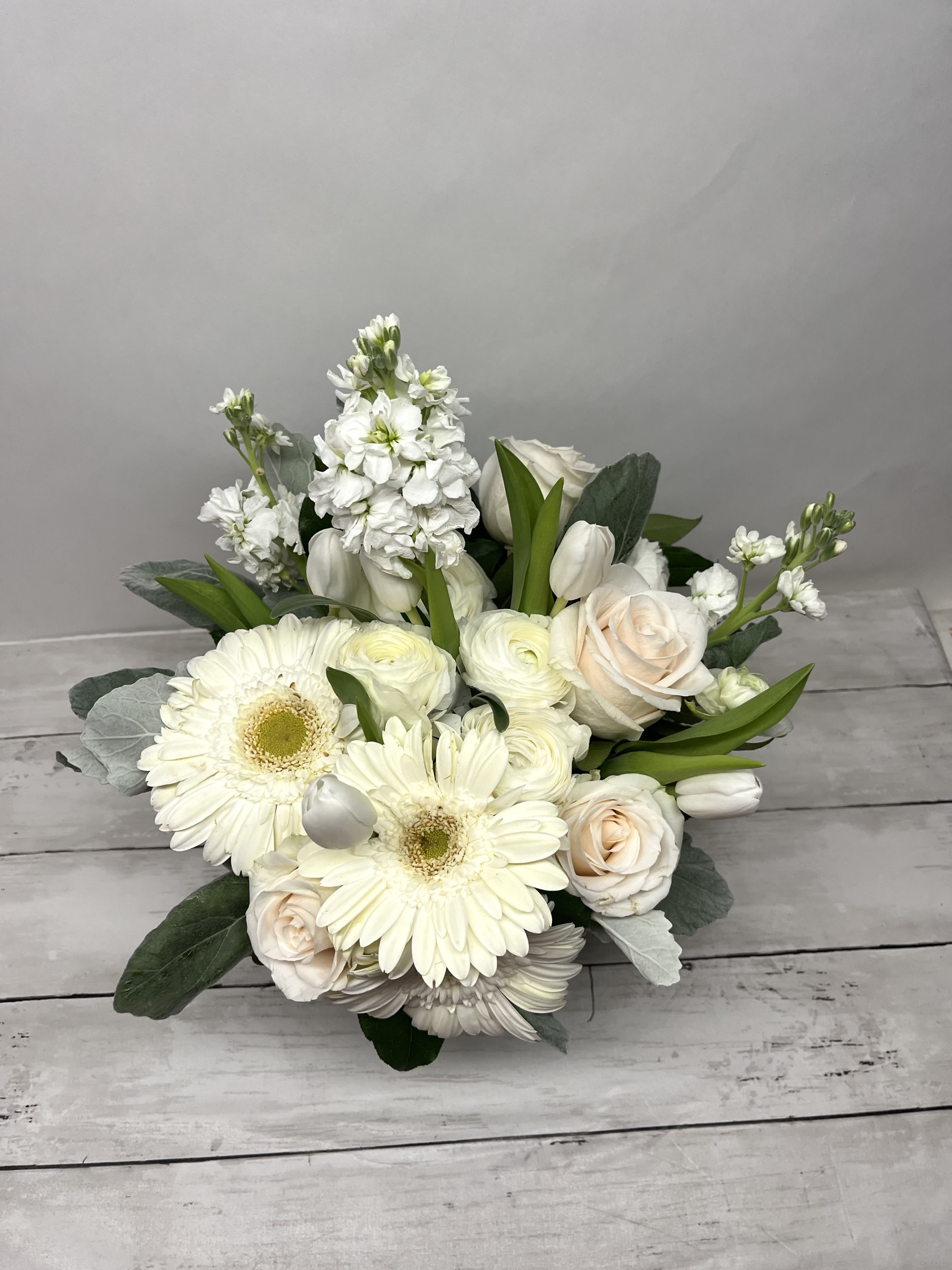 Purity by BloomNation™ - This arrangement contains gerbera daisies, roses, tulips, stock, and other seasonal blooms. APPROXIMATE DIMENSIONS: 15" D x 13" H