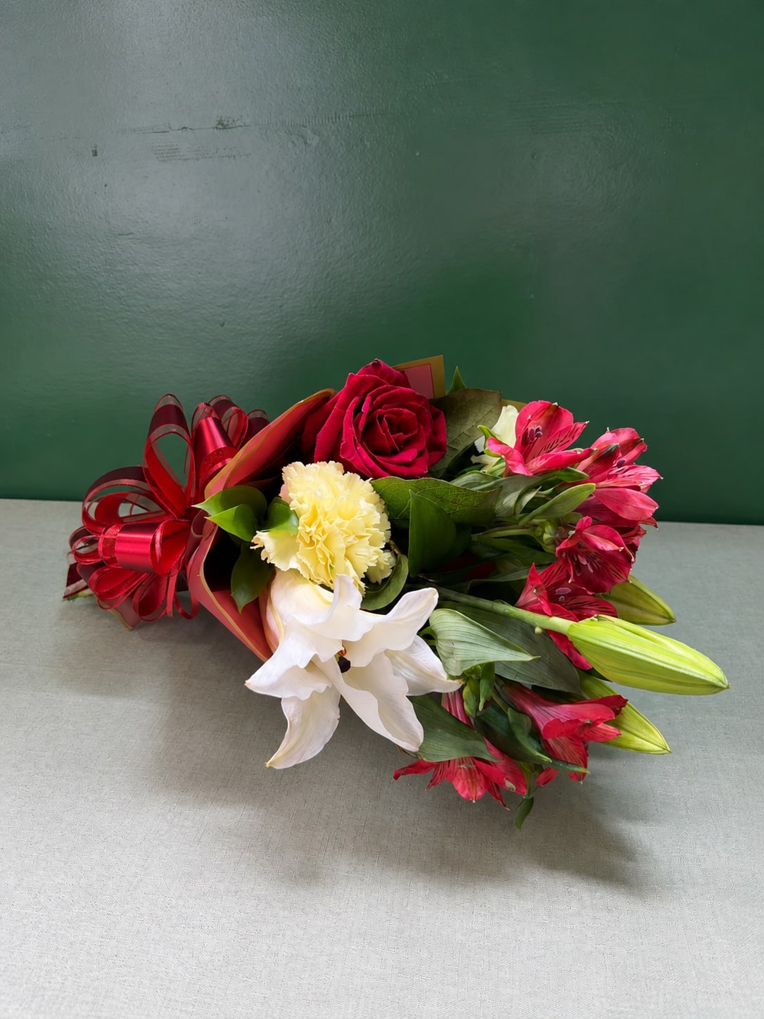 Bouquet of red roses, white lilies, and pink alstroemeria with a red ribbon