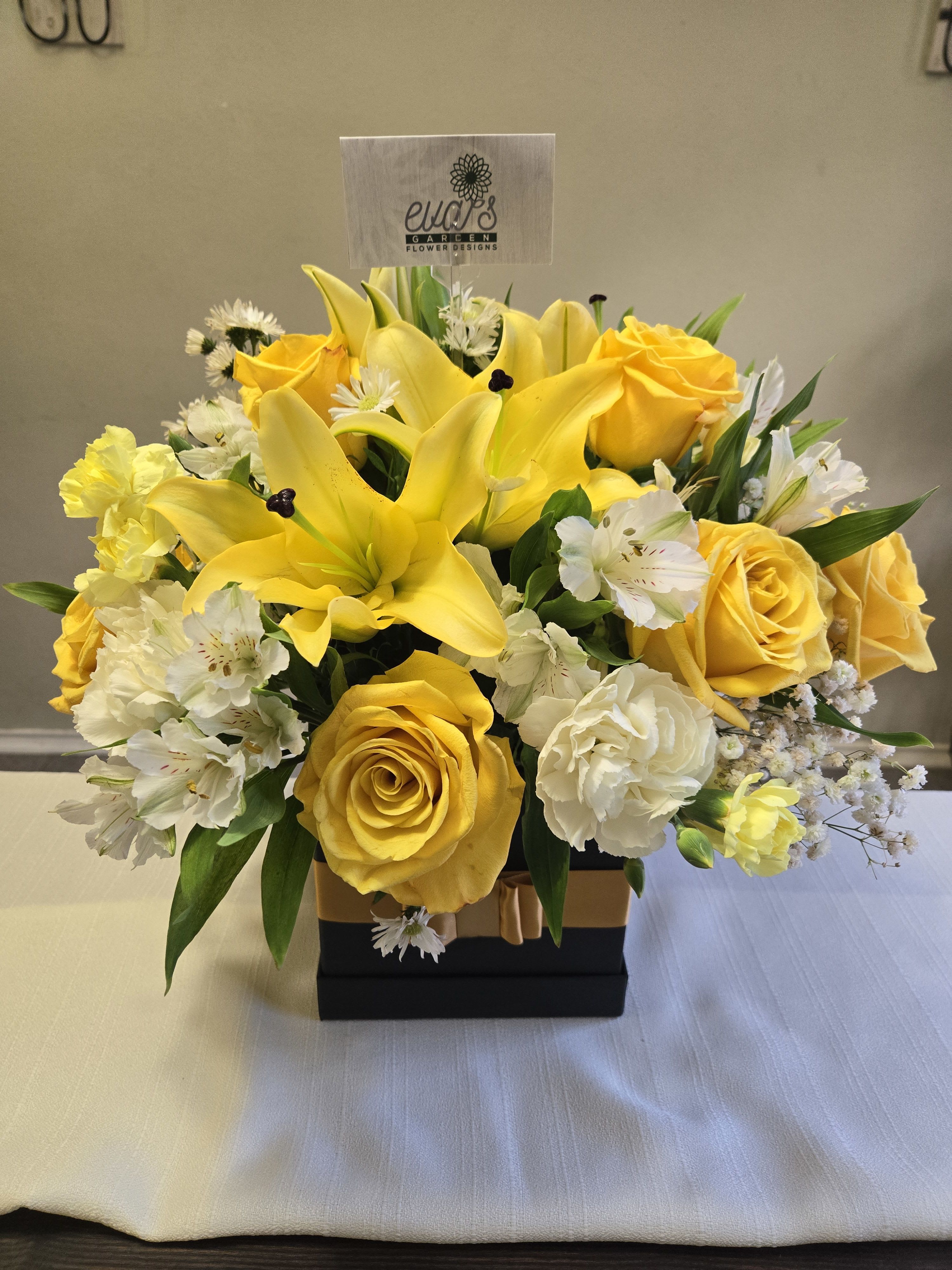 Yellow roses and lilies arranged in a black box with white accents