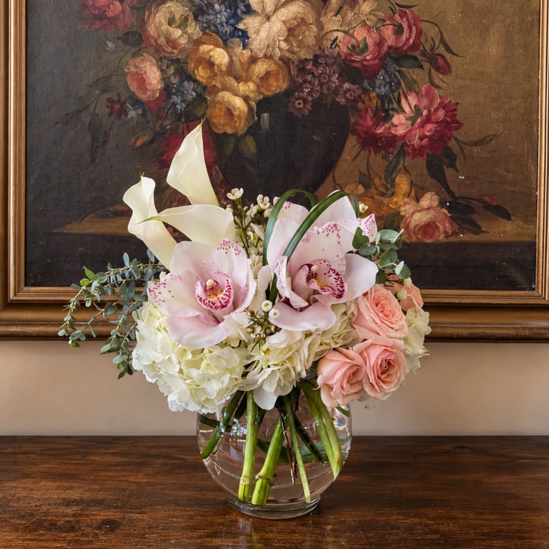 Pink orchids and roses in a clear glass vase with white hydrangeas