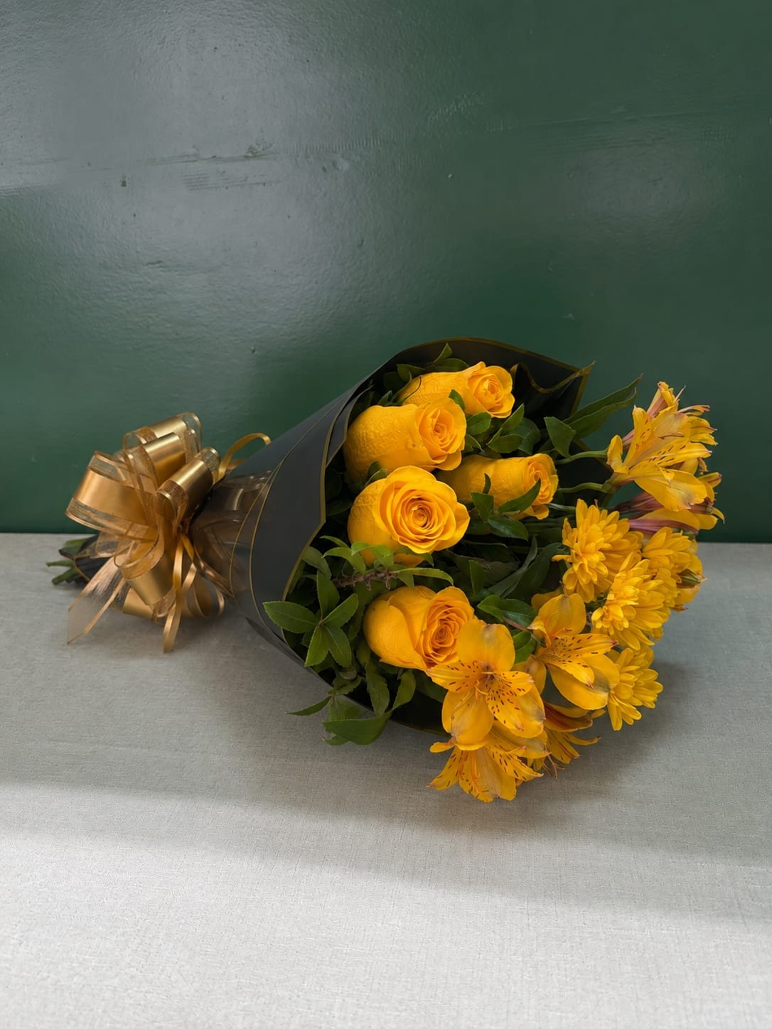 Yellow roses and yellow flowers wrapped in black paper with a gold bow