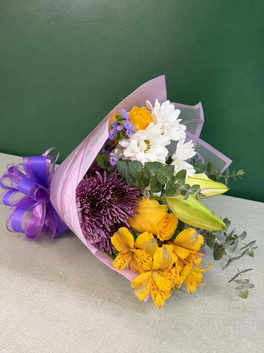 Bouquet of yellow, white, and purple flowers wrapped in pink paper