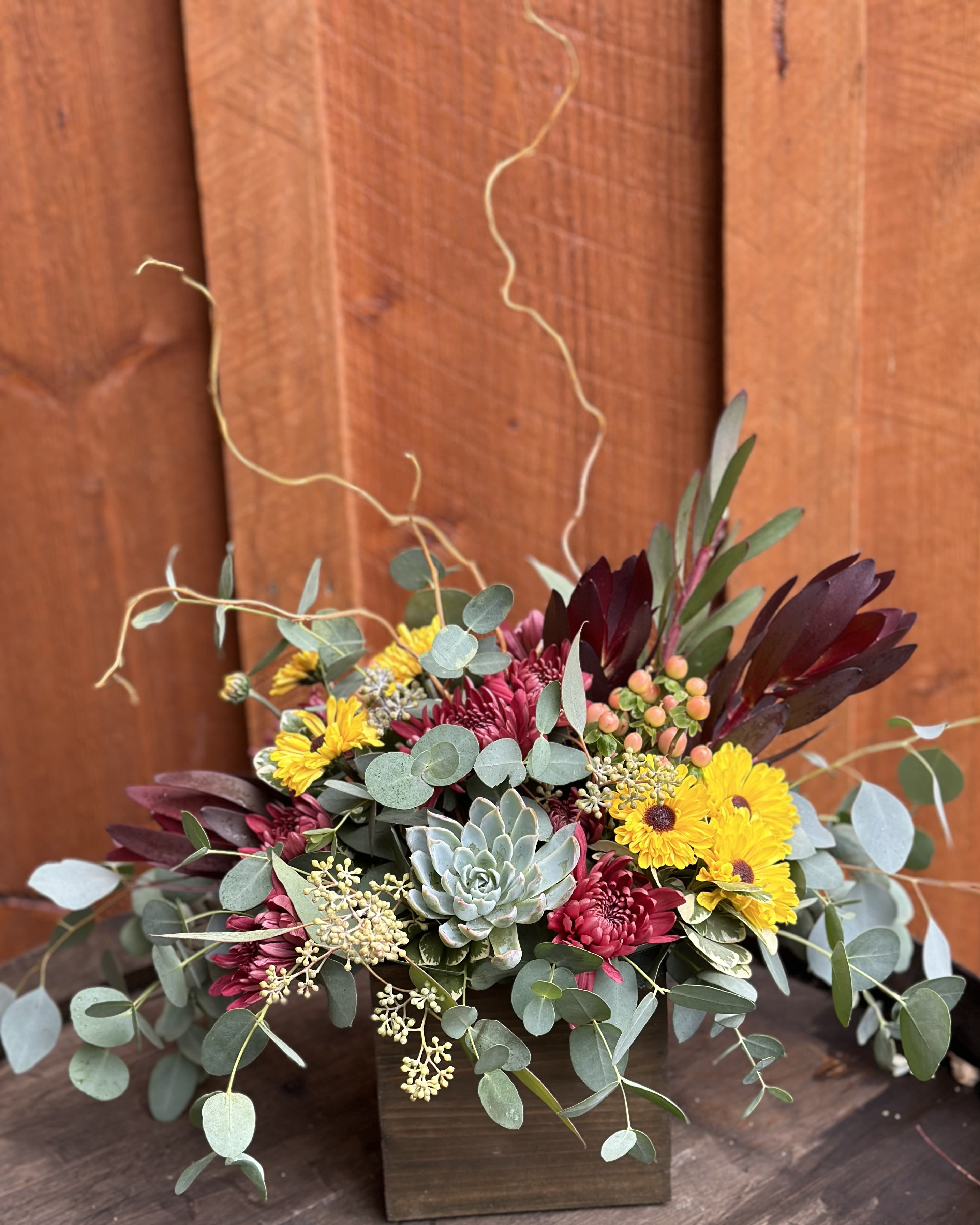 Mixed bouquet with yellow daisies, burgundy blooms, and a succulent in a wooden box