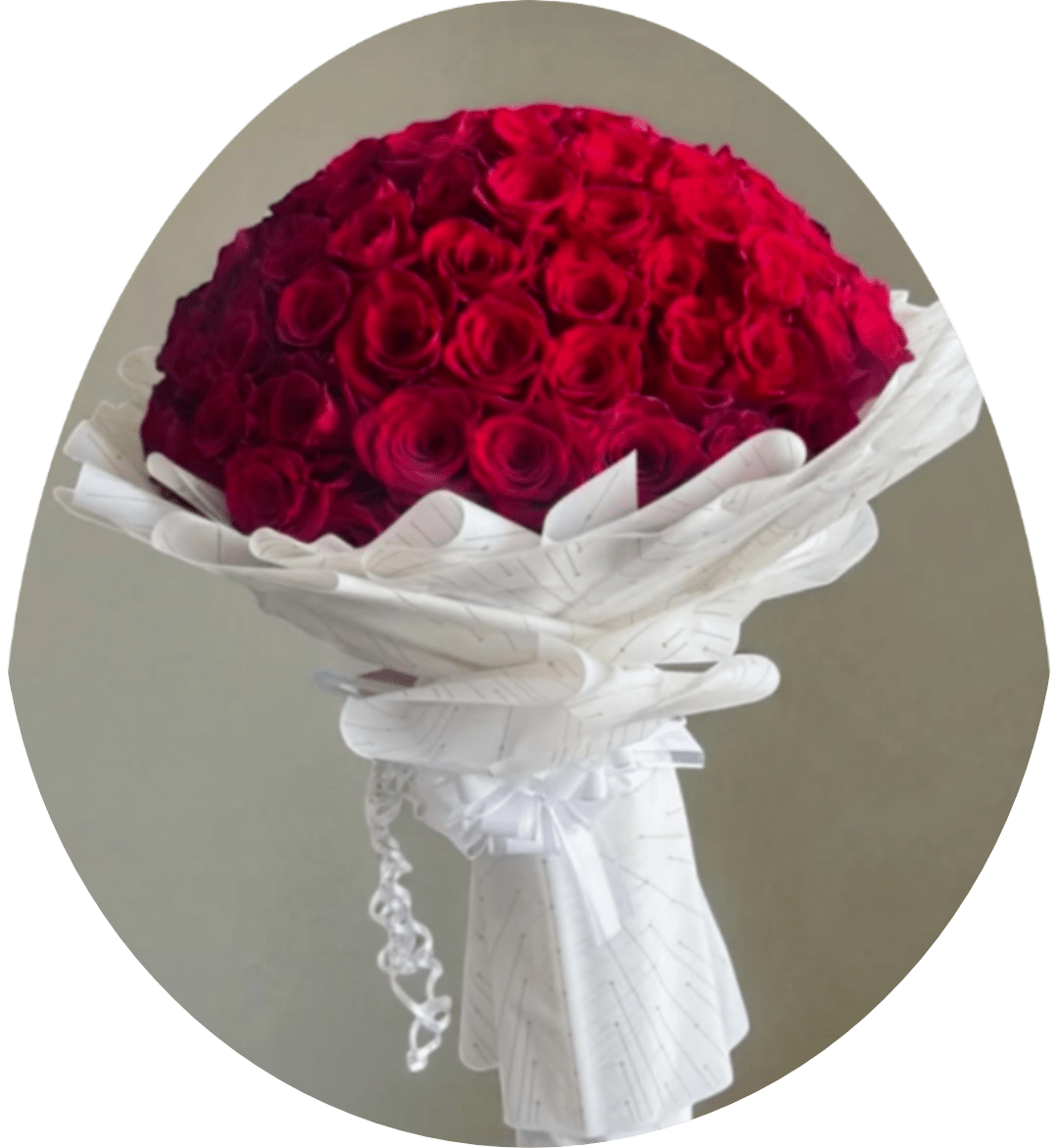 Anastacia Red and White Rose Bouquet - A breathtaking dome of deep red roses wrapped in crisp white paper-this red rose bouquet is designed for anniversaries, Valentine's Day, or any love-centered celebration. The saturated crimson blooms packed into a rounded, full shape create an immediate, romantic impact; the white wrapping and tied ribbon sharpen the contrast and give the arrangement a formal, polished presentation that makes the recipient feel truly cherished.  Each bouquet is hand-tied into a substantial, tightly packed dome and finished with layered white decorative paper and a coordinating ribbon for a classic, elegant look. Scattered rose petals in the display underscore the celebratory mood and dramatic color contrast. Ideal for saying "I love you," marking a milestone, or surprising the person you're thinking of, this arrangement arrives ready to impress-full, fragrant, and made to make someone feel deeply seen.