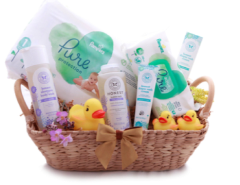 New Baby Gift Basket With Rubber Ducks and Toiletries - A cheerful baby gift basket that feels like a warm welcome for a newborn-perfect for a baby shower or to celebrate the arrival of a little one. This baby gift set is presented as a shallow woven wicker basket tied with a tan satin bow, combining practical baby-care items with playful accents to create a joyful, usable keepsake for new parents.  The basket includes assorted baby toiletries and care product containers in white packaging with pastel green and purple labels, plus multiple bright yellow rubber ducks and small decorative flowers tucked around the base. A fabric bow and satin ribbon finish the presentation, and the soft palette of white, yellow, pink, green, and purple gives the set a gentle, celebratory look that reads as both thoughtful and practical.  Give this as a newborn gift that says you're thinking of both baby and parents-a lovely way to provide useful essentials while adding a touch of charm to the nursery. The woven basket can be reused for storage, and the arrangement arrives ready to present with its tan bow and neat packaging; ideal for same-week gifting to celebrate births or baby showers.