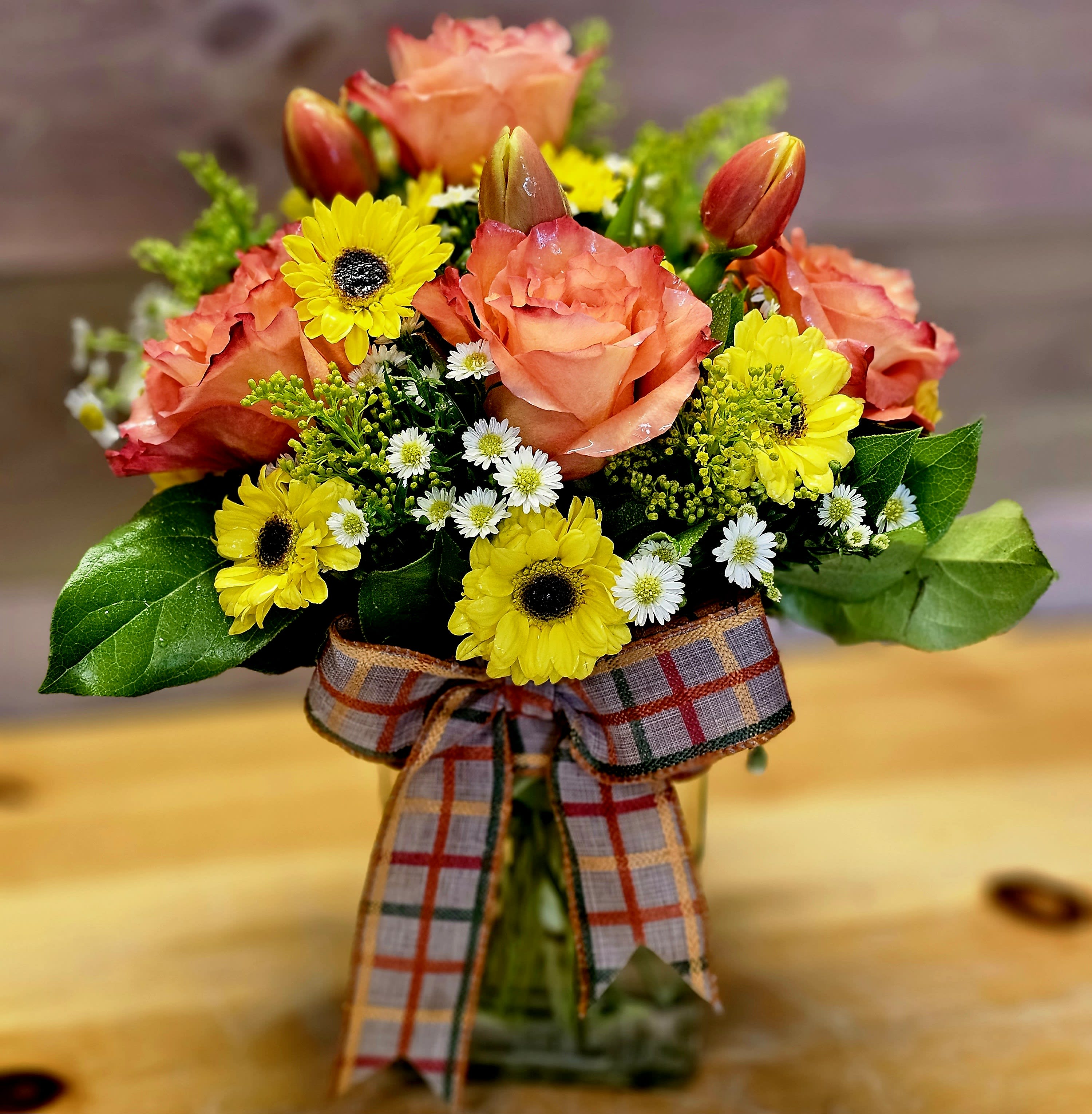 Bouquet of peach roses and yellow daisies in a glass vase with a plaid ribbon