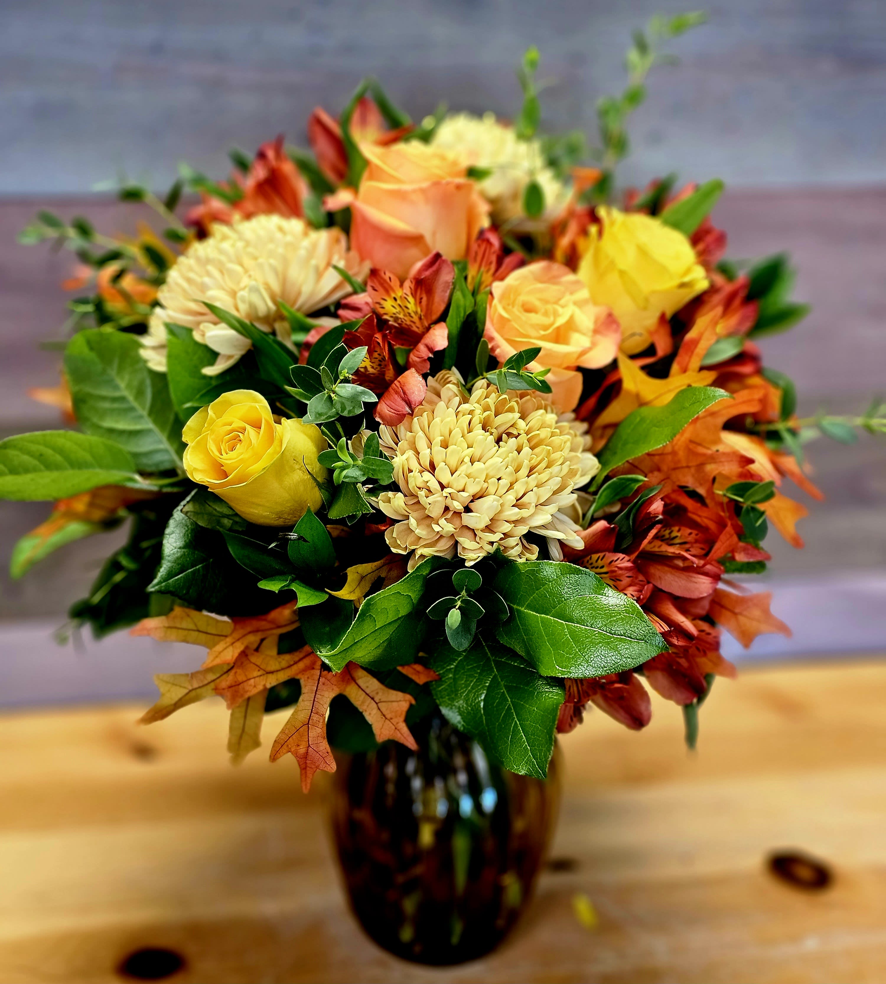 Bouquet of yellow and peach roses with orange flowers in a dark glass vase