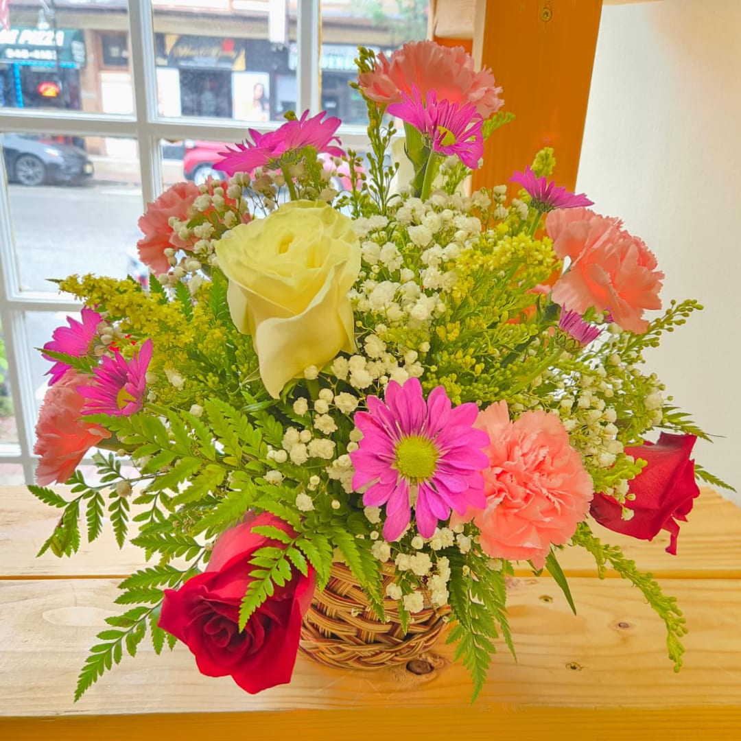 Mixed bouquet in a woven basket with roses, carnations, and daisies
