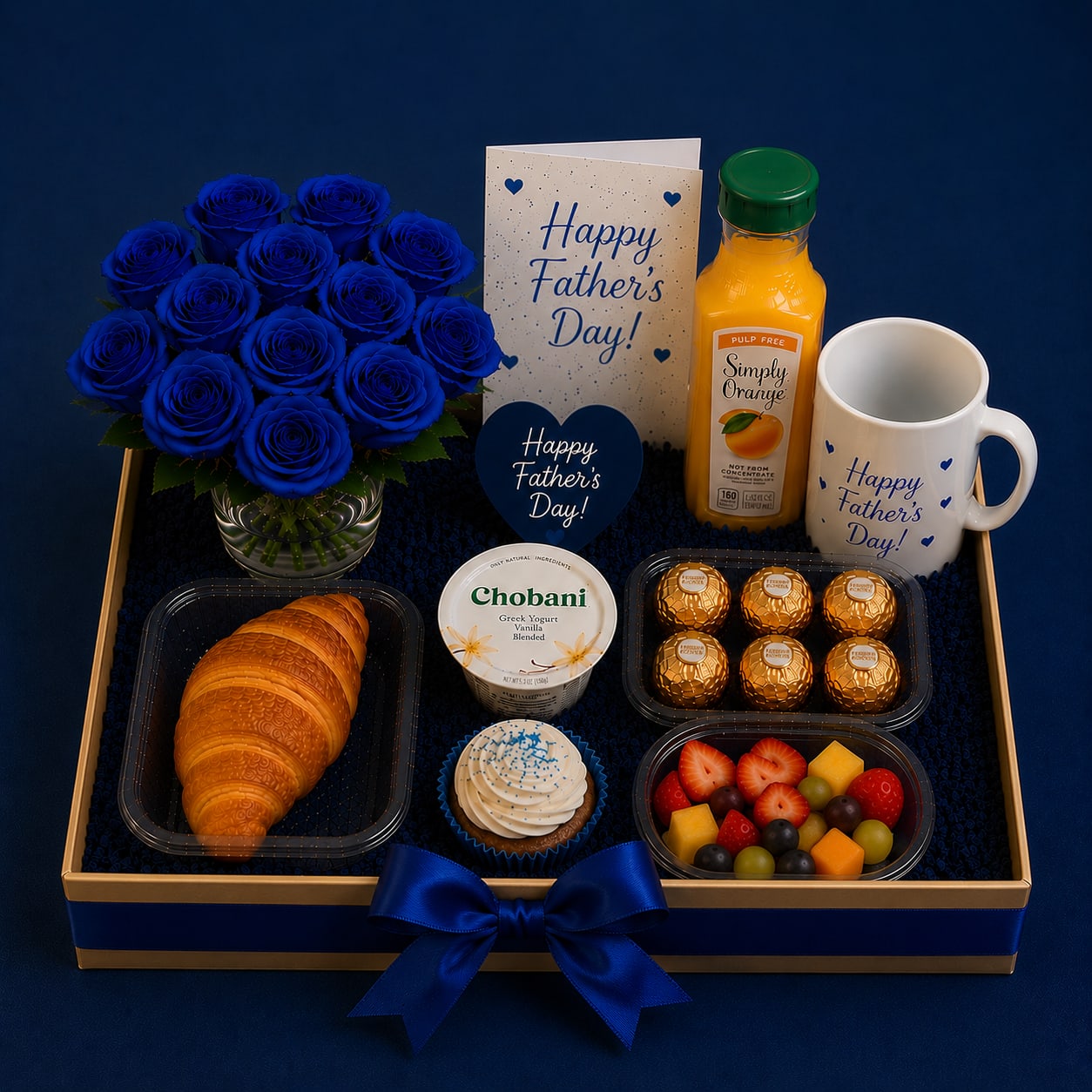 Father's Day Breakfast Gift Arrangement with Blue Roses - Bright cobalt blue roses take center stage in this Father's Day breakfast gift arrangement, paired to feel both celebratory and comfortably masculine - perfect as a Father's Day bouquet or a thank-you gift for the dad you want to pamper. The compact arrangement reads blue-and-white at first glance, so the person you're thinking of will feel seen and celebrated the moment the box is opened. Include a short note on the enclosed greeting card to make the moment personal.  This gift tray pairs vivid blue roses with accents in orange, white, and yellow and arrives in a polished glass vase tucked inside a gift box with satin ribbon. Alongside the flowers you'll find a ceramic mug, a bottle of orange juice, a frosted cupcake, croissants, yogurt, a chocolate box, and a fruit-and-cheese snack assortment organized in plastic compartments for an indulgent breakfast experience. The presentation is coordinated and neat: a juice bottle and pastries sit beside the roses, with the greeting card displayed so your message is front and center.  Give this to a dad who deserves a relaxed start to his day - new fathers, grandfathers, or the coworker finishing a big project - and let the combination of fresh blue roses and tasty morning treats do the celebrating. Care is simple: keep the roses in their vase water and refresh as needed for lasting color, and order in advance for reliable delivery in Miami, FL.