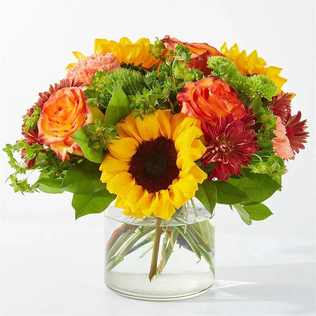 Bouquet of sunflowers, roses, and chrysanthemums in a clear glass vase