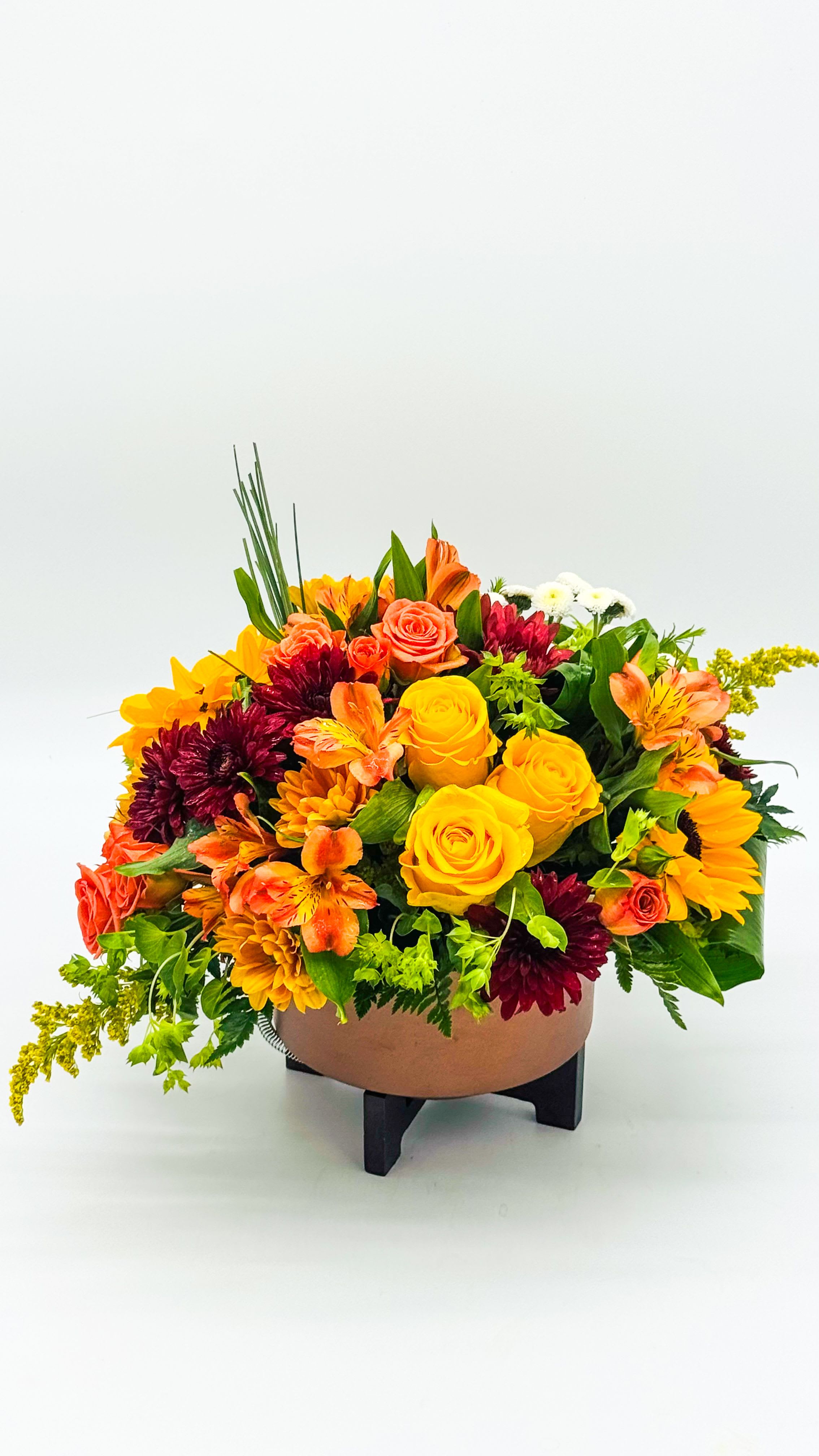 Autumn Copper Serenade - Autumn Copper Cascade: A lush cluster of fall-colored blooms and greenery gathered in gleaming copper containers. Rich amber, burnt orange, and deep burgundy blossoms mingle with earthy greens, while delicate foliage weaves through the stems, creating a cascading, garden-fresh look. The warm metallic sheen reflects autumn light, adding a sophisticated glow to any table or entryway.