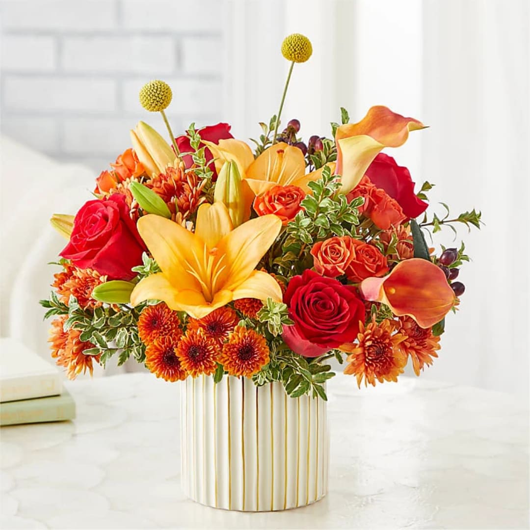 Scarlet Skies Bouquet - Bright, warm color and a full, rounded silhouette make this flower arrangement a joyful choice for birthdays, anniversaries, or a cheerful thank-you. The Scarlet Skies bouquet pairs vivid red roses and orange calla lilies with golden lilies, rust-toned chrysanthemums, and orange spray roses so the recipient will feel celebrated and energized the moment they see it.  Perfect for someone who loves bold color, this compact yet abundant display works well for general celebration, congratulations, or to brighten a room just because. Vase-prepared for immediate display; simple care-fresh water and a cool spot-will keep the flowers looking their best.
