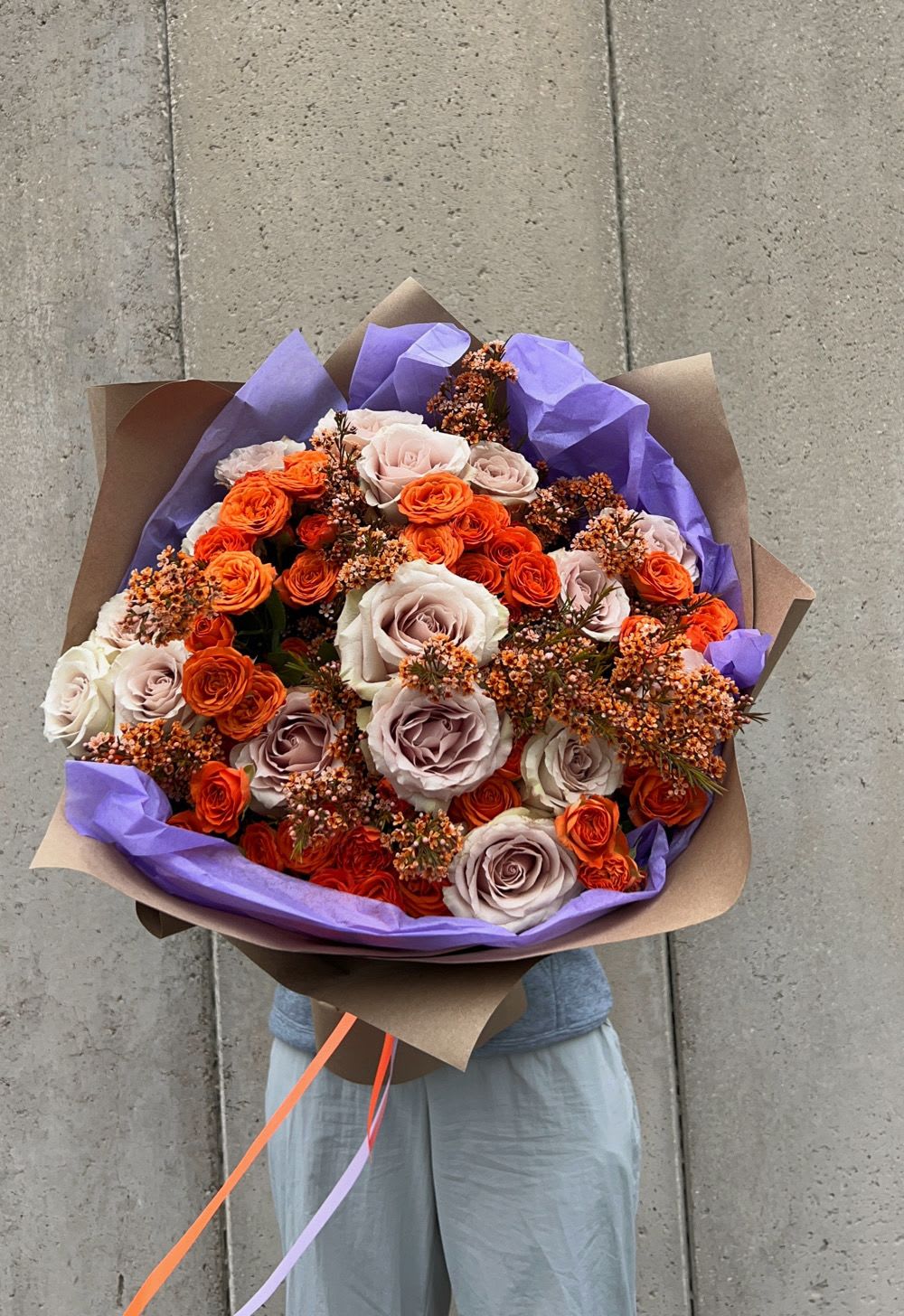 Bouquet of orange and blush roses wrapped in purple paper