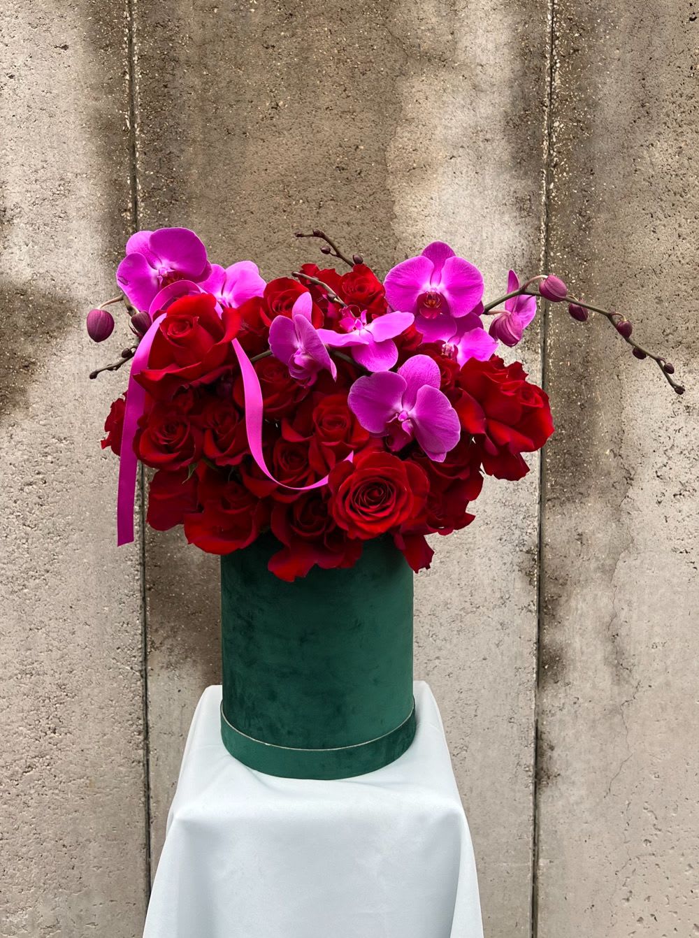 Red roses and pink orchids in a green hatbox