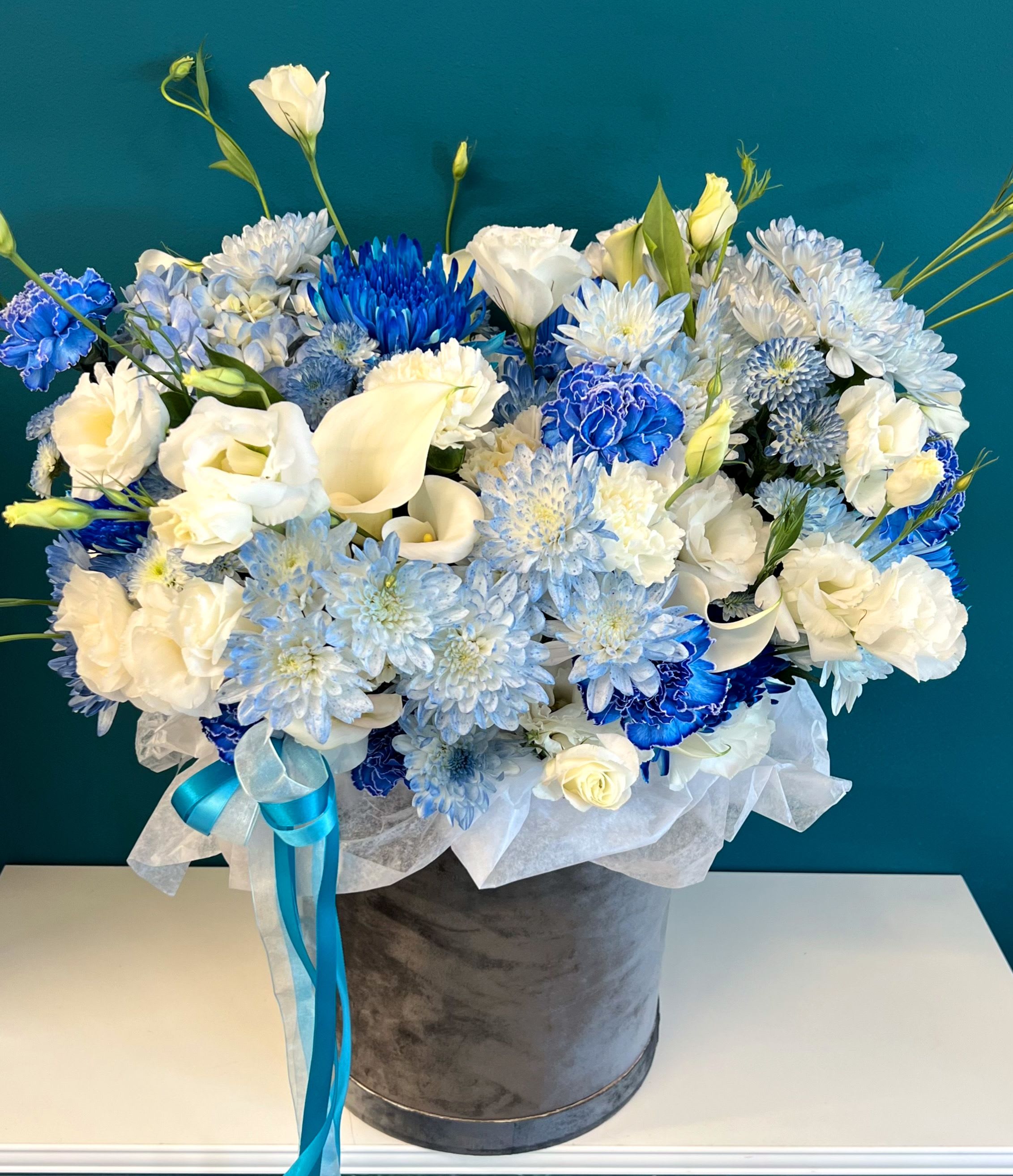Blue and white floral arrangement in a gray hatbox with ribbon