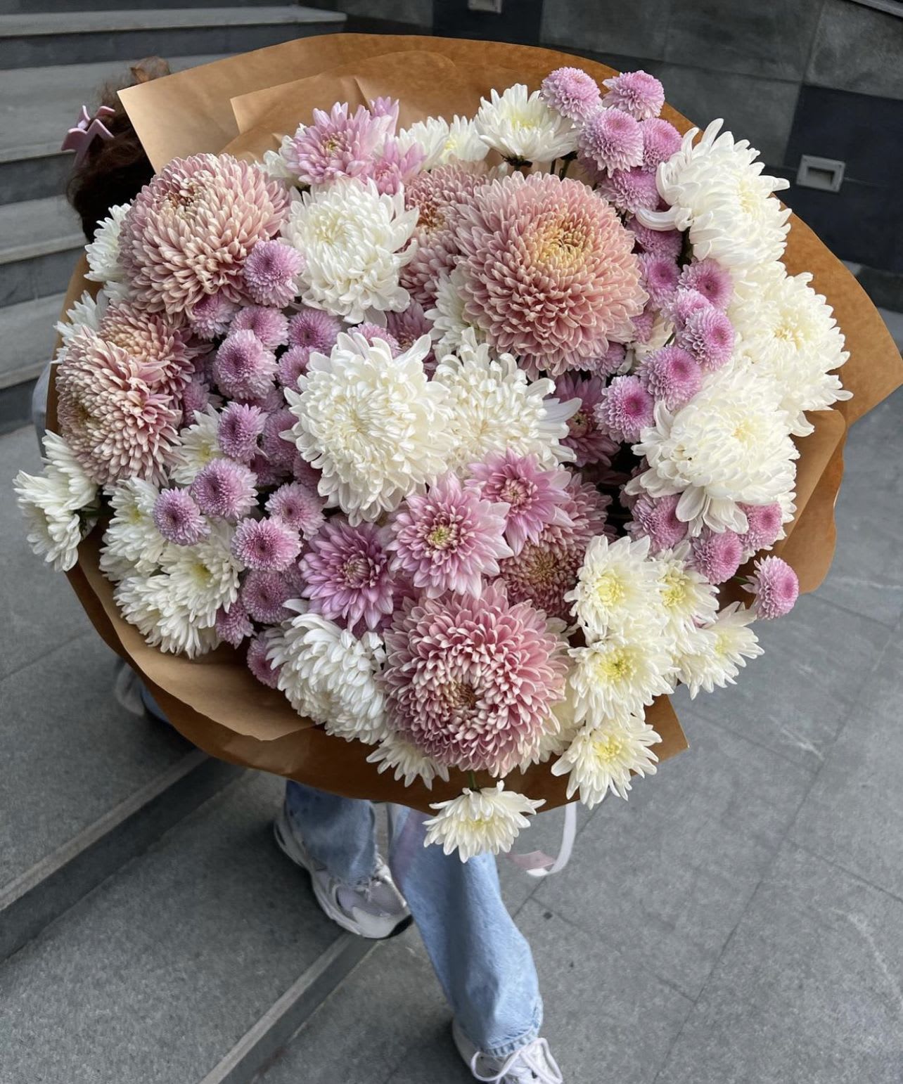 Large bouquet of pink, white, and lavender chrysanthemums wrapped in brown paper