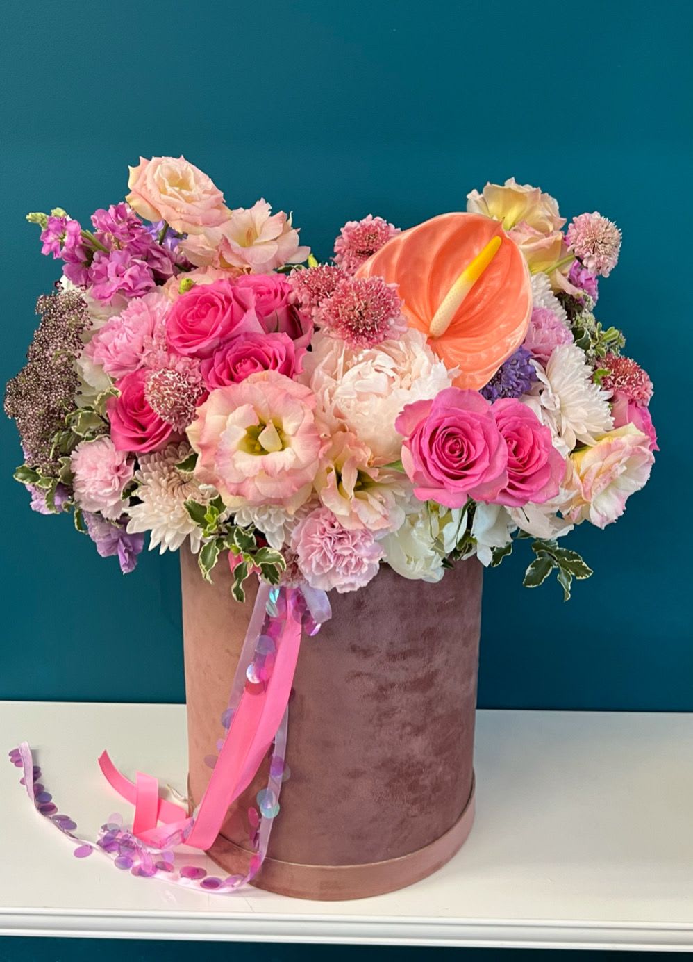 Pink and peach floral arrangement in a velvet hatbox with ribbon