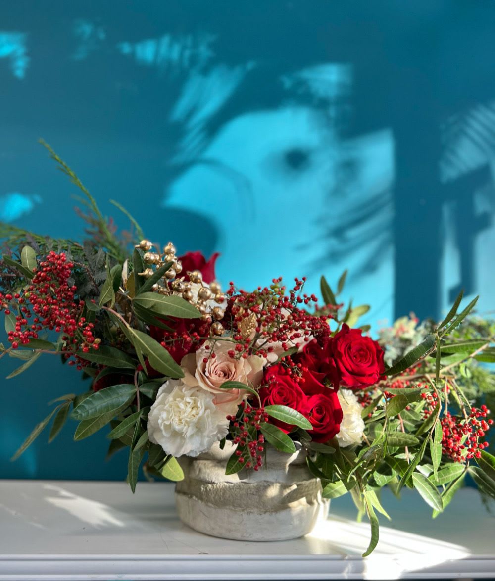 Red and white roses arranged in a low stone vase with berries