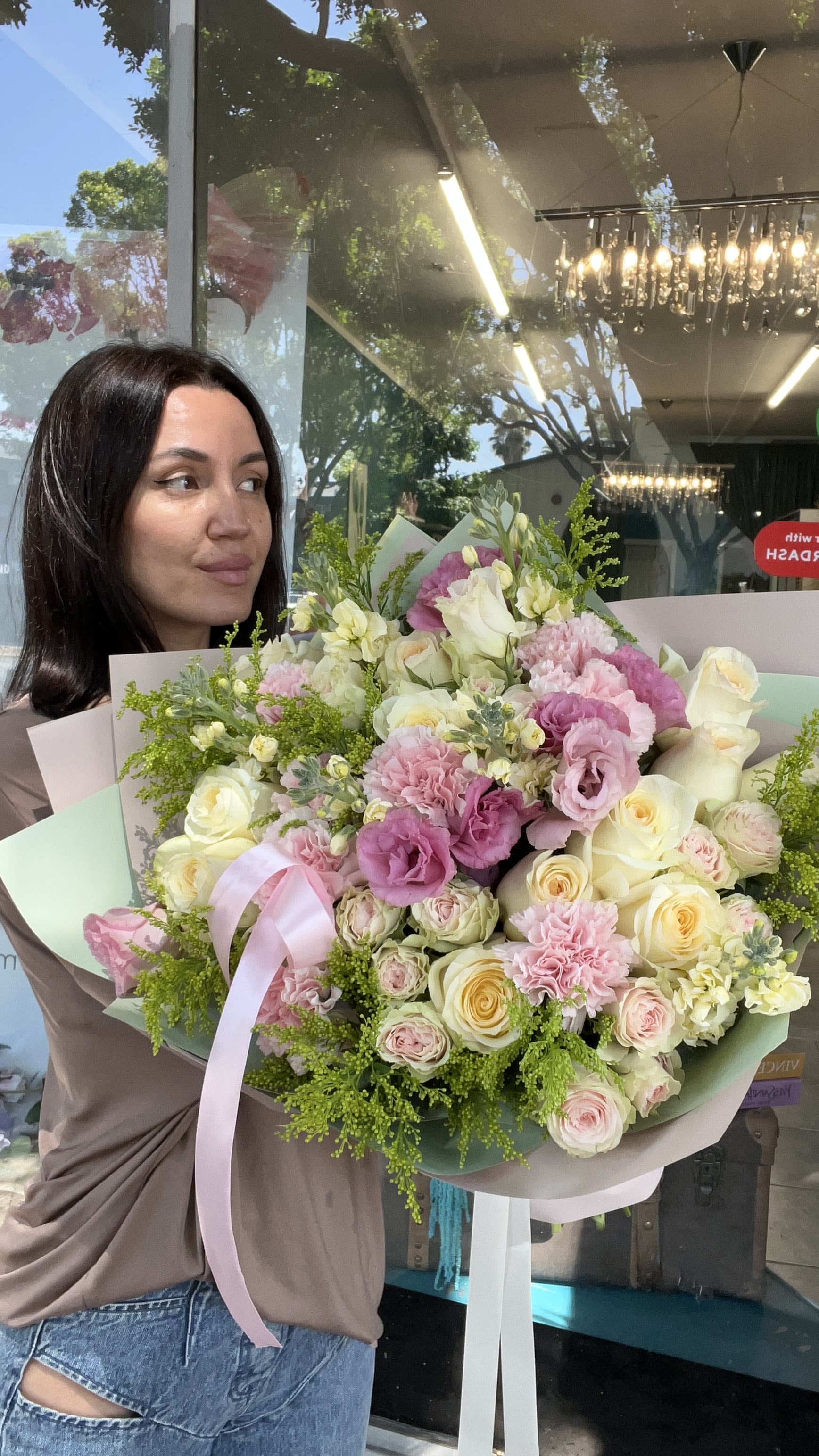 Woman holding a large bouquet of pink and cream flowers with a ribbon