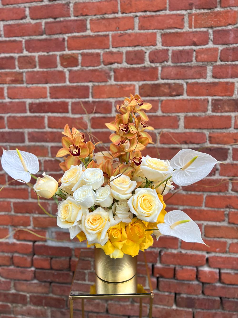 White and yellow roses with orange orchids in a gold vase