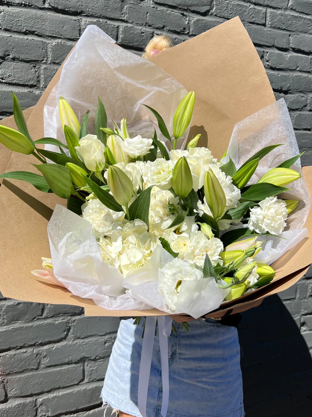 Large bouquet of white lilies and carnations wrapped in kraft paper