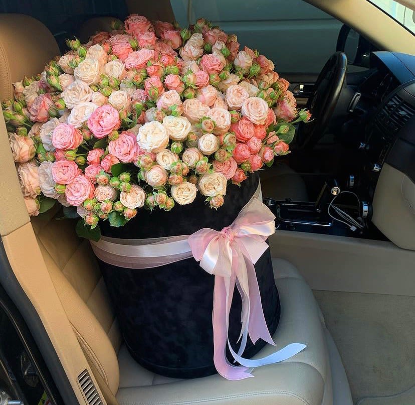 Large bouquet of pink and white roses in a black hat box with a pink ribbon