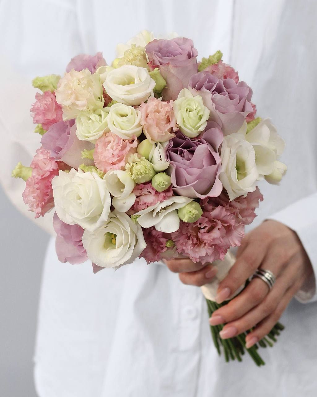 Handheld bouquet of blush, lavender, and white roses with pink ruffled blooms