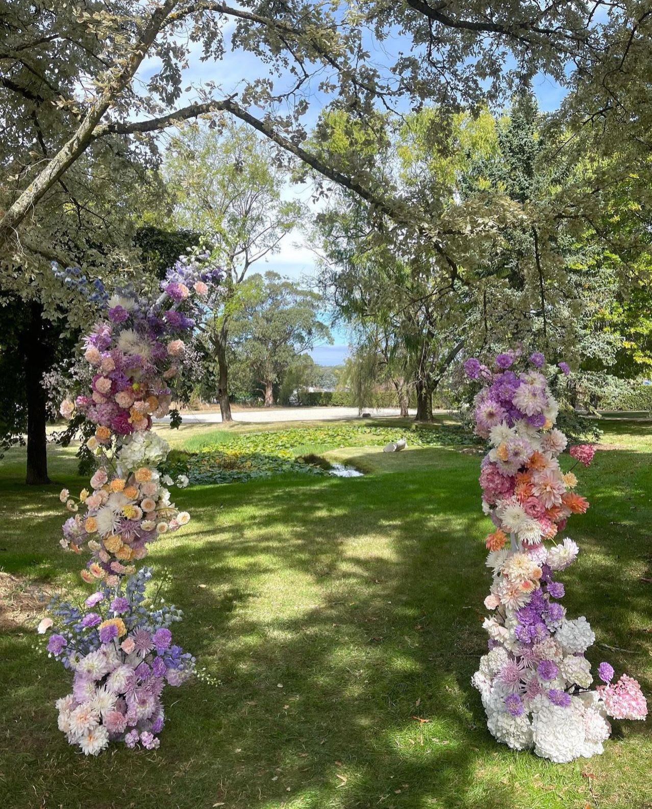 Two tall floral columns in pastel purple, pink, and white outdoors
