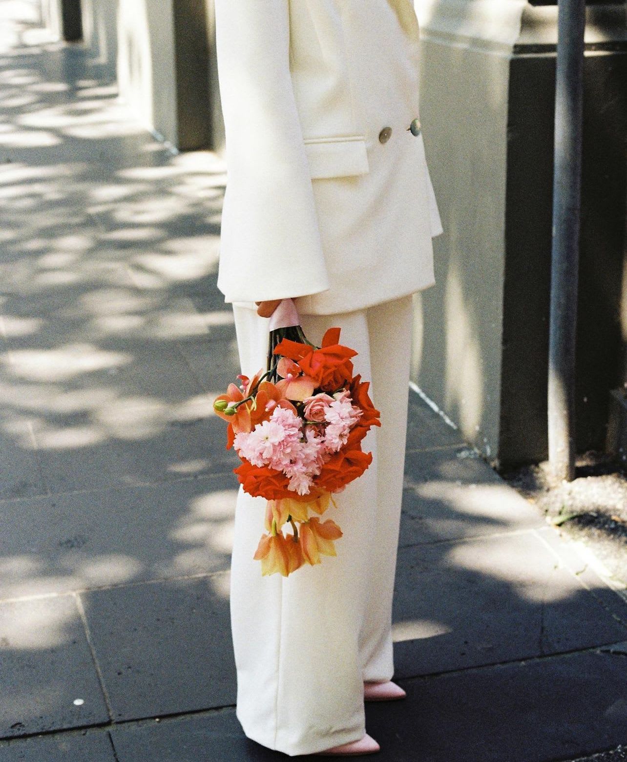 Person in white suit holding a colorful bouquet of pink and orange flowers