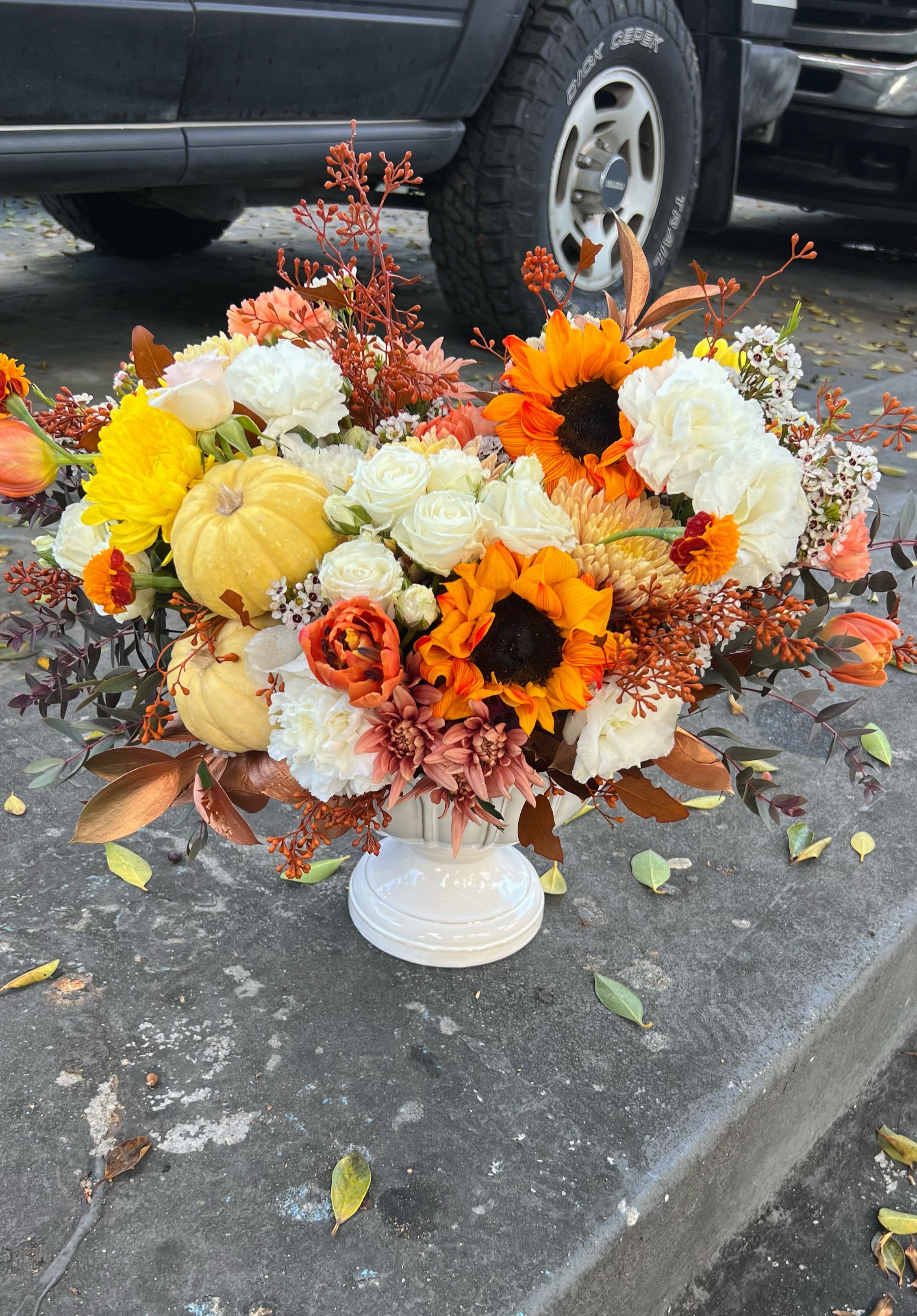 Autumn floral arrangement with sunflowers, white roses, and pumpkins in a white vase
