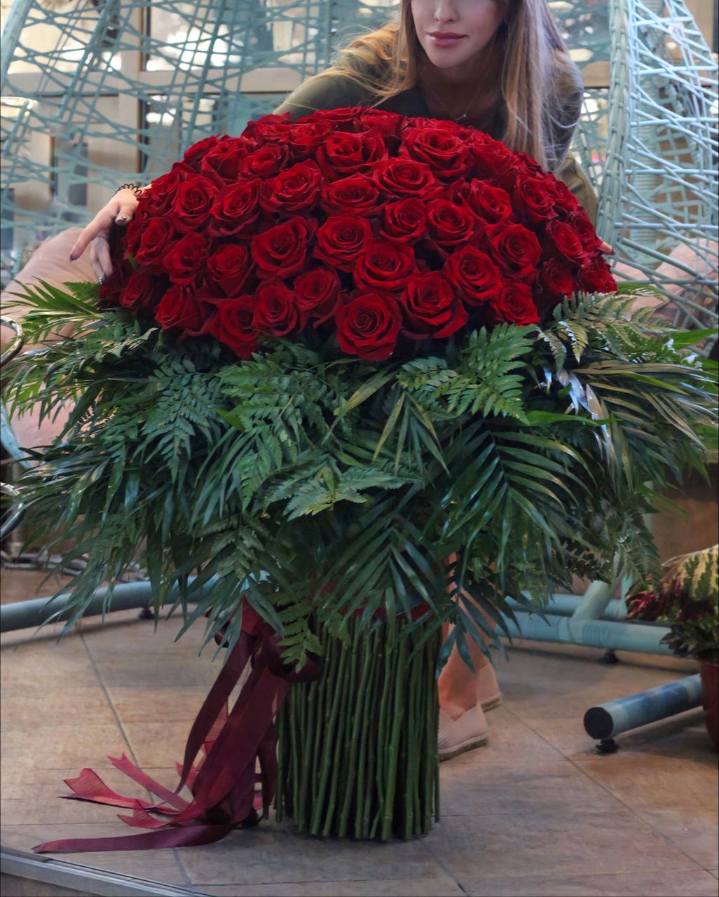 Large bouquet of red roses with dark greenery and ribbon