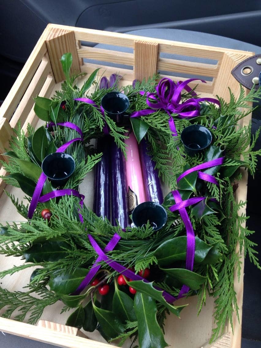 Evergreen wreath with purple ribbon and candle holders in a wooden crate
