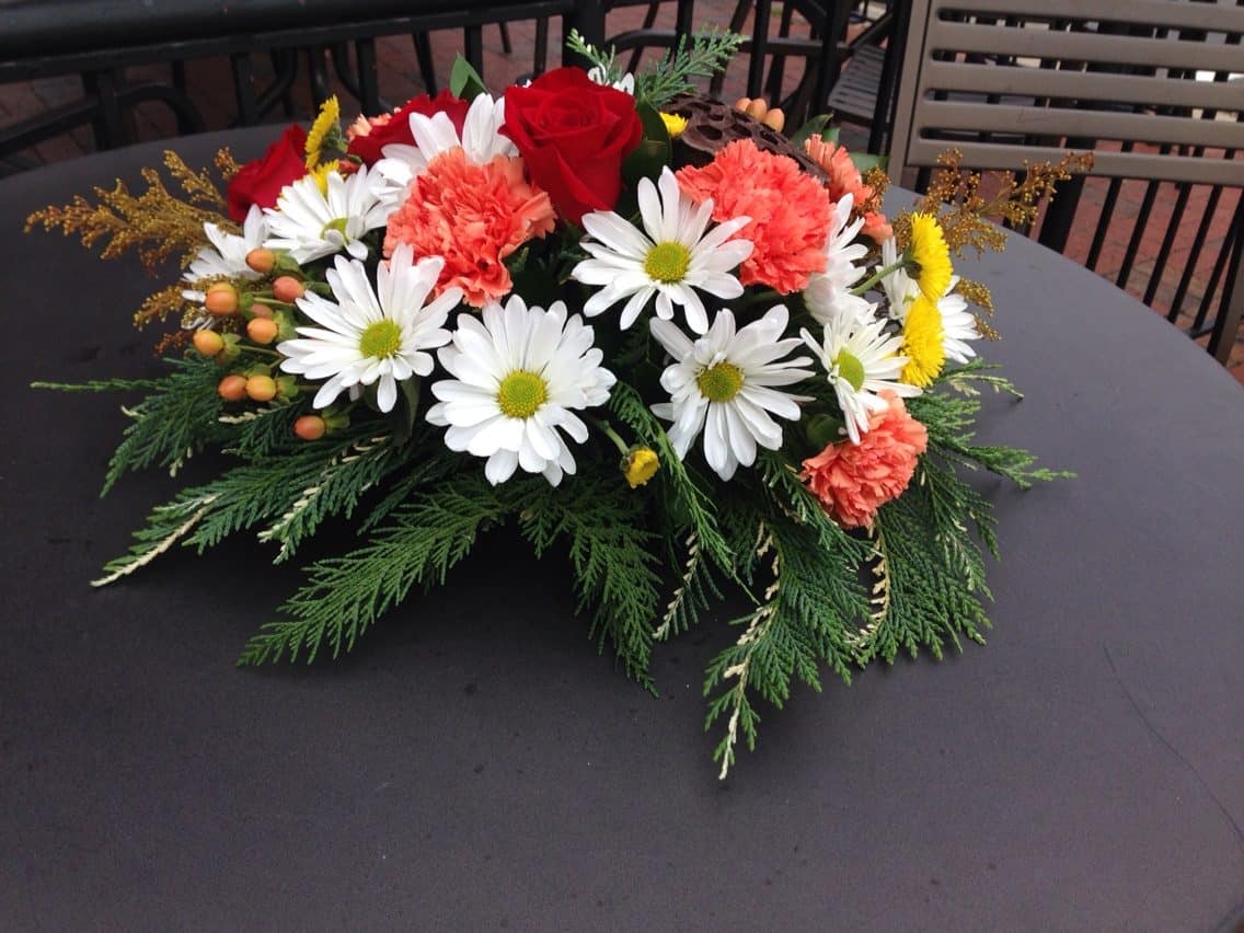 Low floral centerpiece with red roses, white daisies, and coral carnations