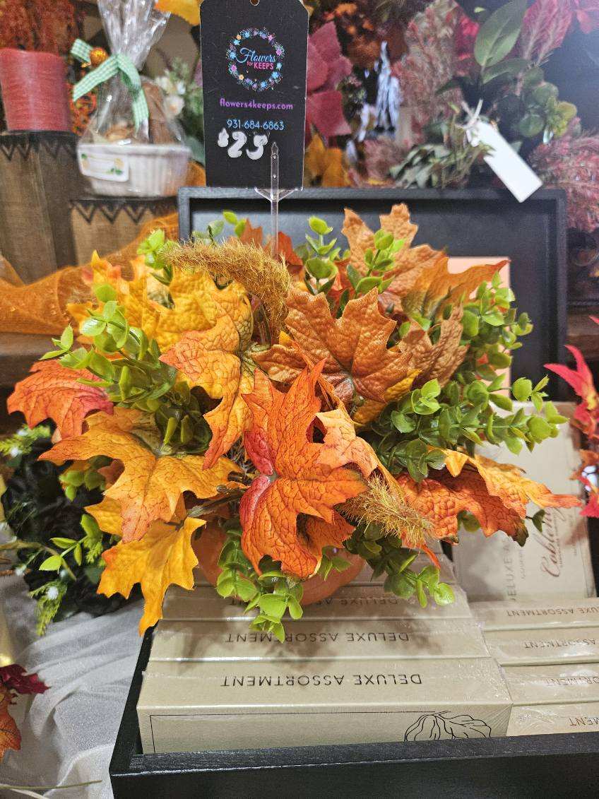 Autumn arrangement with orange maple leaves and green foliage in a container.