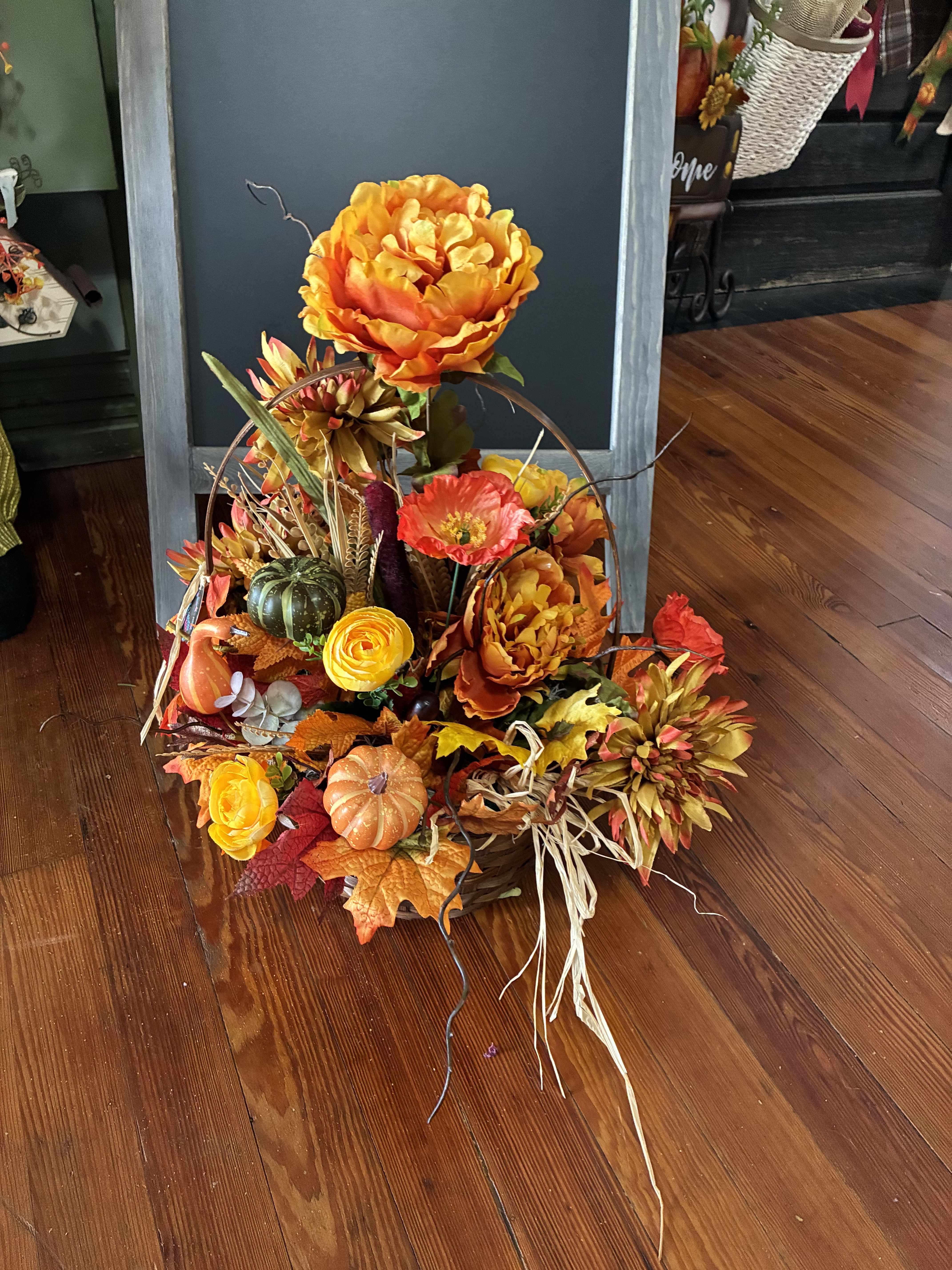 Autumn floral arrangement with orange blooms, pumpkins, and fall leaves in a basket.